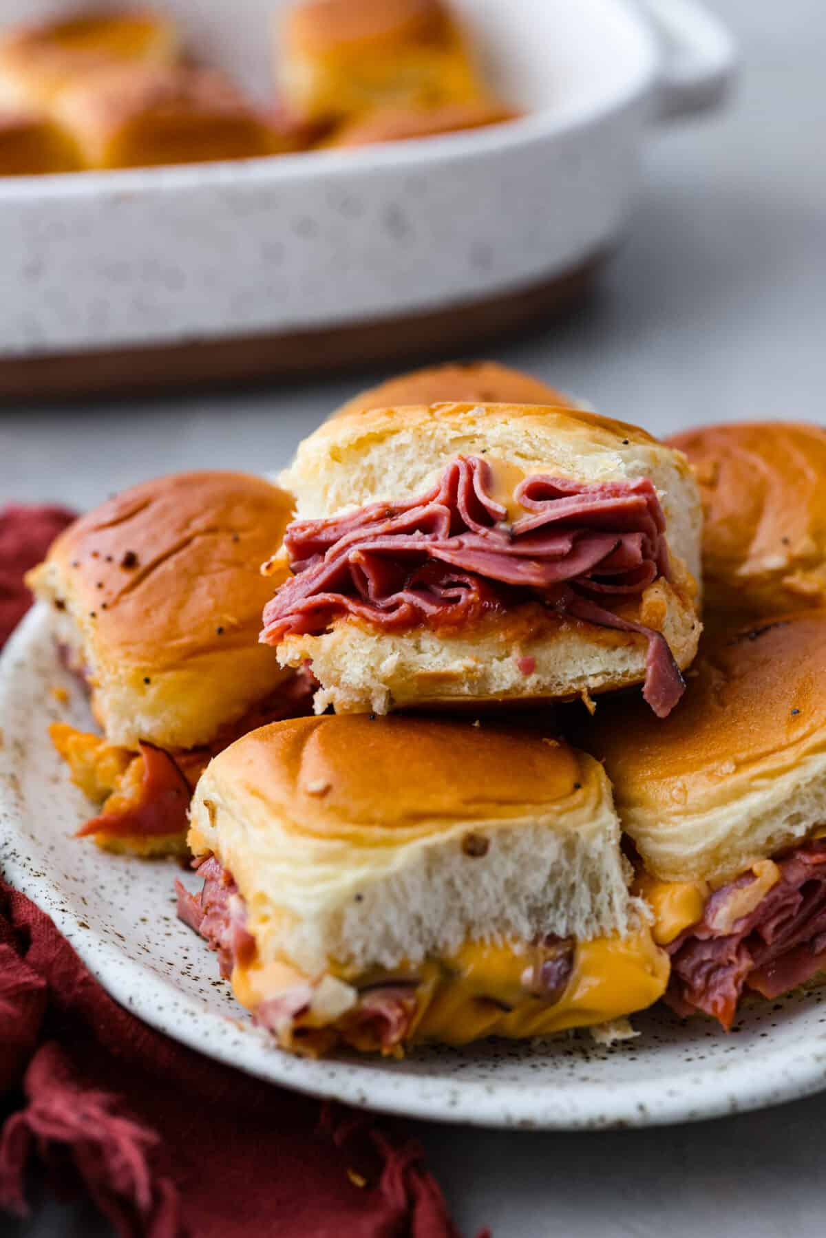 These copycat Arby's beef and cheddar sliders are a must-make for your next gathering. Soft Hawaiian buns topped with sliced roast beef, melty American cheese, onion flakes, and homemade Arby's sauce, brushed with a buttery glaze. Beef and cheddar sliders served on a plate.