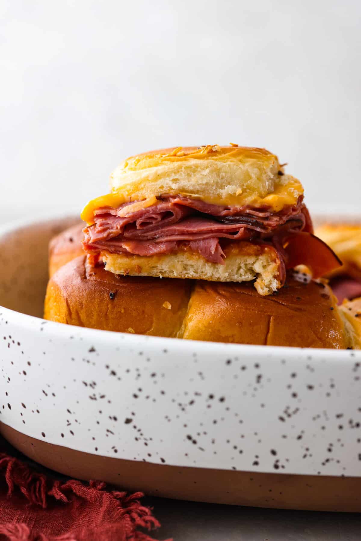 These copycat Arby's beef and cheddar sliders are a must-make for your next gathering. Soft Hawaiian buns topped with sliced roast beef, melty American cheese, onion flakes, and homemade Arby's sauce, brushed with a buttery glaze. Beef and cheddar sliders stacked on top of each other.