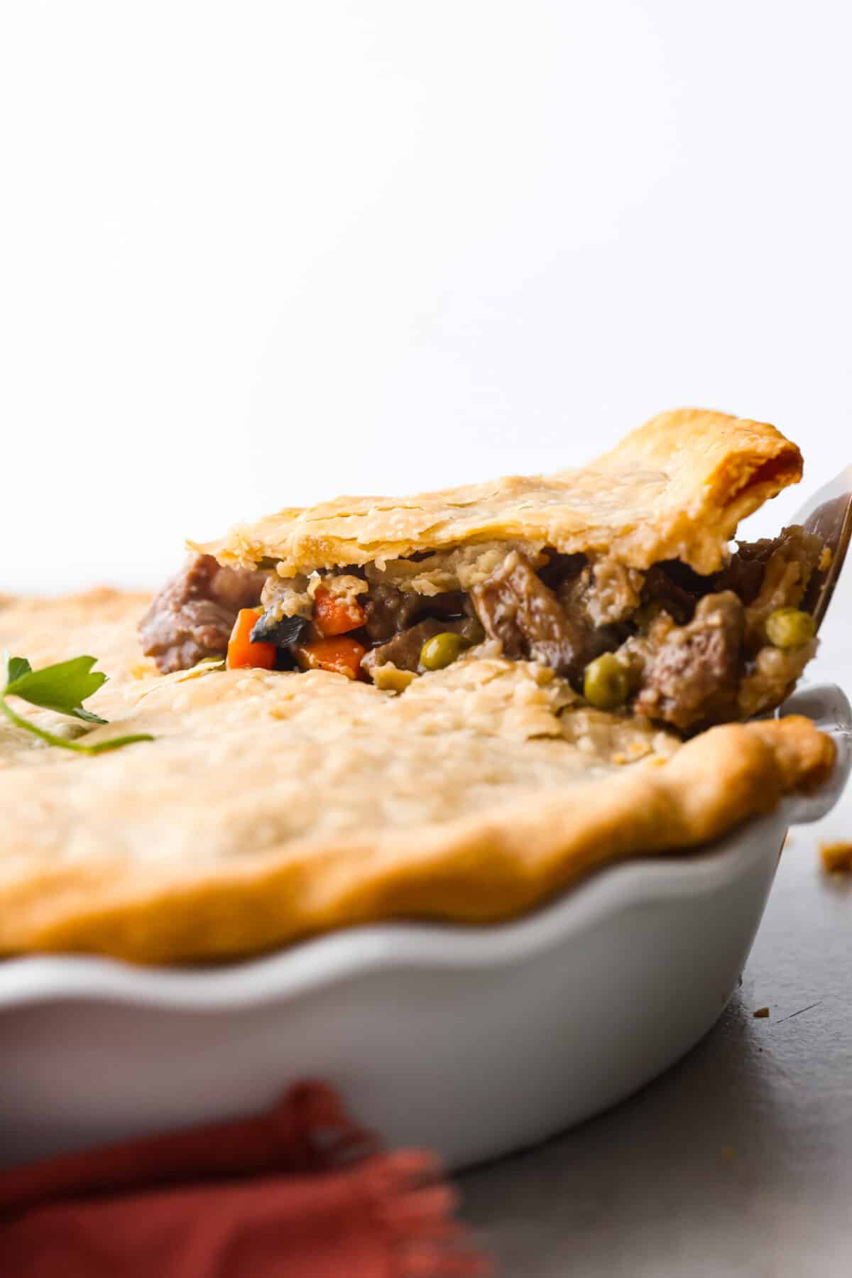 Classic comfort food with a homemade twist! This hearty beef pot pie features tender chunks of beef, savory veggies, and a rich gravy all nestled in a flaky double crust! (You can use store-bought crusts for easy prep!) Lifting a piece of beef pot pie out of a baking dish.