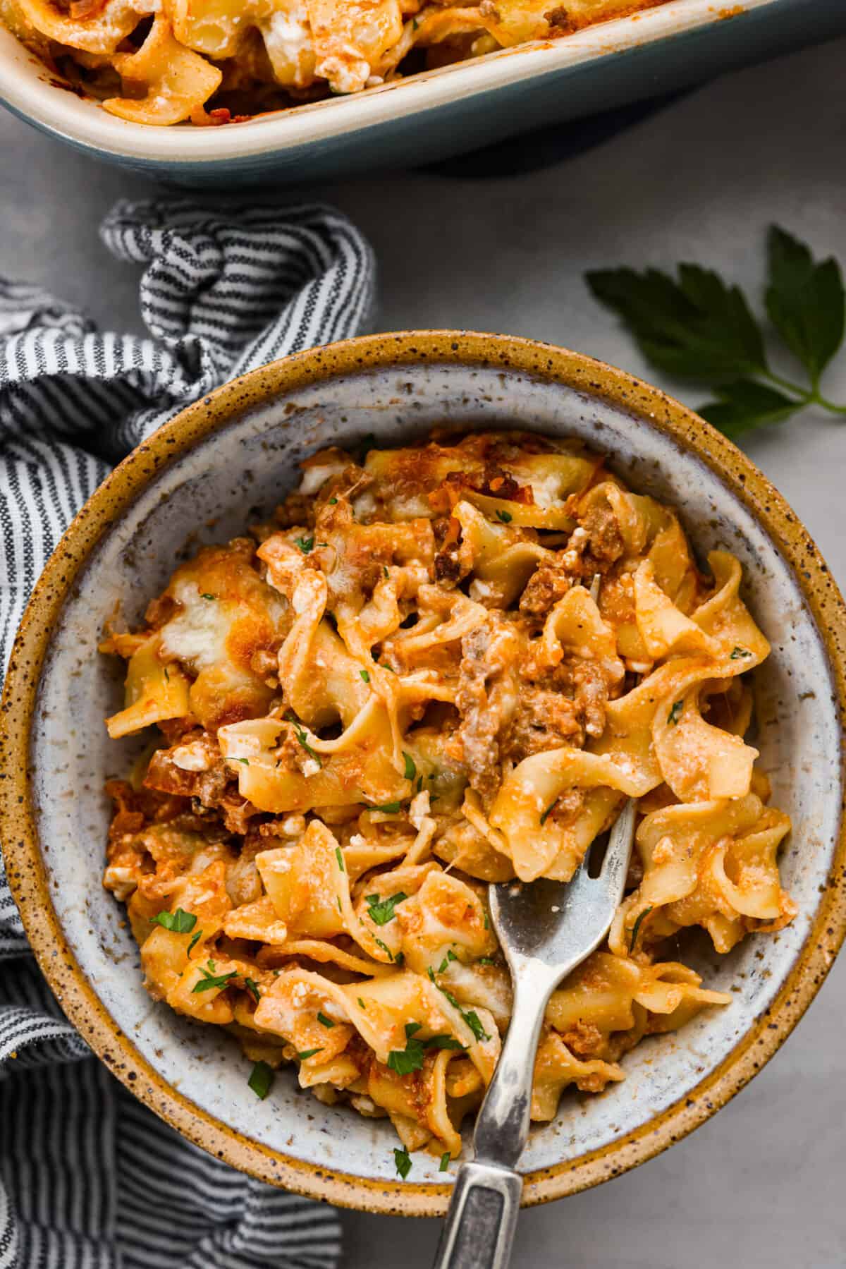 This flavorful Sour Cream Noodle Bake takes pasta to a whole new level! Using sour cream, cottage cheese, ground beef, tomato sauce, noodles and plenty of mozzarella, this recipe will have you coming back for seconds and even thirds! A serving of some sour cream noodle bake in a stoneware bowl.
