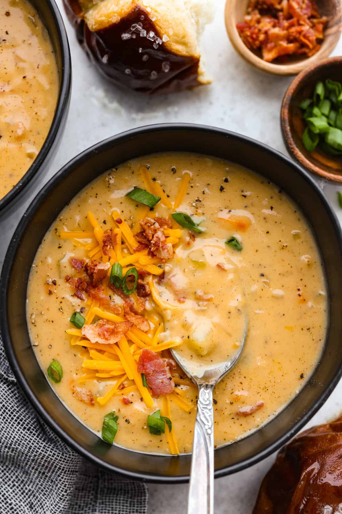 If you're looking for a hearty and comforting soup that's also packed with flavor, this beer cheese soup checks all the boxes! It's made with simple ingredients like bacon, vegetables, and cheese, and the beer adds a subtle depth of flavor that will have you coming back for seconds. Top-down view of beer cheese soup in a black bowl, topped with shredded cheese, bacon bits, and chopped green onions.