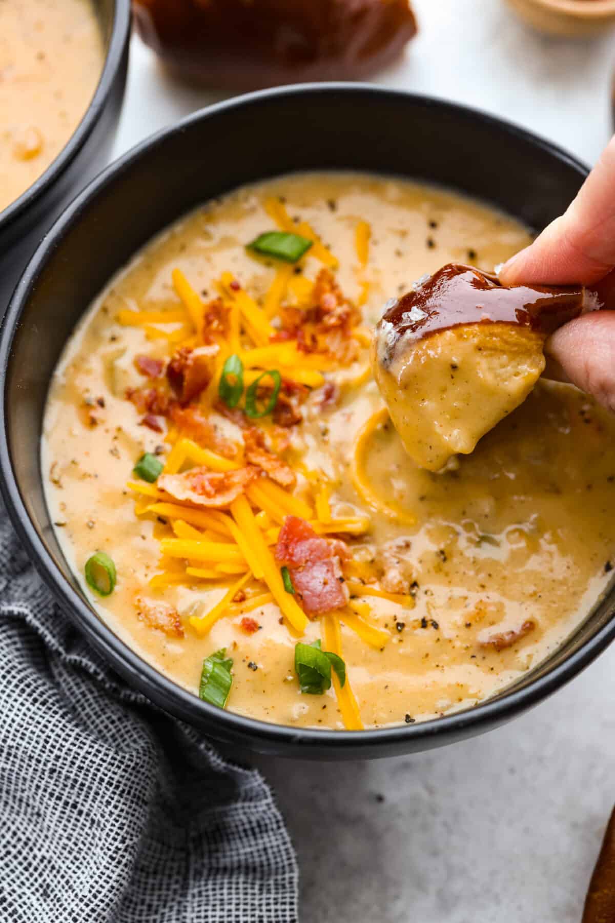 If you're looking for a hearty and comforting soup that's also packed with flavor, this beer cheese soup checks all the boxes! It's made with simple ingredients like bacon, vegetables, and cheese, and the beer adds a subtle depth of flavor that will have you coming back for seconds. Dipping a pretzel roll into the soup.