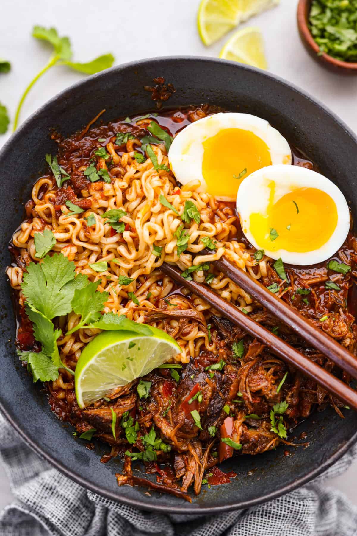 My Birria Ramen is next-level delicious! Tender shredded chuck roast, rich consommé, and slurp-worthy noodles all in one bowl. Birria ramen topped with a soft boiled egg, lime, and cilantro.