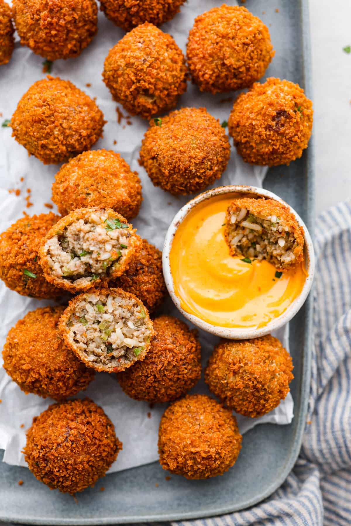 Crispy on the outside and perfectly tender inside, Boudin Balls are a Cajun classic! A seasoned mixture of sausage, veggies, and rice is formed into balls, then breaded and fried until deliciously crisp and golden. Overhead shot of boudin balls on a serving platter with half of one dipped in sauce.