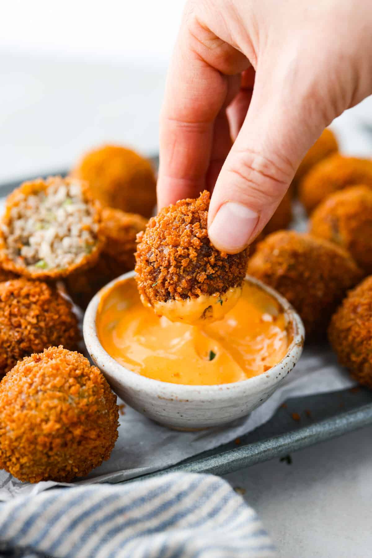 Crispy on the outside and perfectly tender inside, Boudin Balls are a Cajun classic! A seasoned mixture of sausage, veggies, and rice is formed into balls, then breaded and fried until deliciously crisp and golden. Close up shot of someone dipping a boudin ball in sauce.