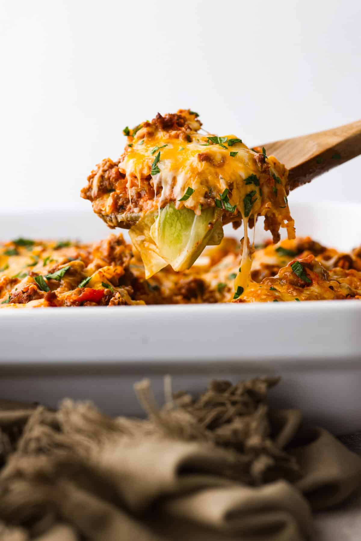 Cabbage roll casserole is a much EASIER version of cabbage rolls! Layers of ground beef, onion, garlic, rice, marinara, cheese, and tasty seasonings are assembled into a casserole. You'll love all the textures and flavors in this easy one-pan dinner! Close side view of a wood spoon lifting up a serving of cabbage roll casserole.