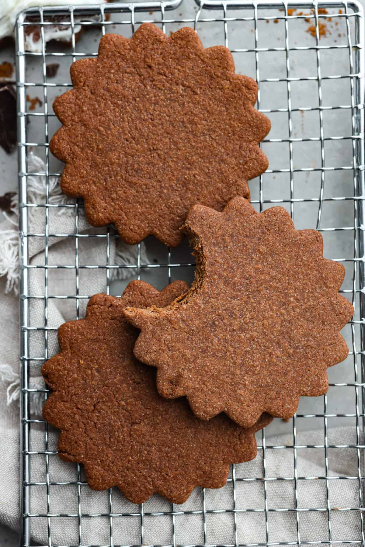 Chocolate sugar cookies are buttery, tender and melt in your mouth with each delicious bite! These are the perfect elevated cookies to cut out and frost for Valentine's Day, or any day! 3 cookies on a wire rack. One has a bite taken out of it.