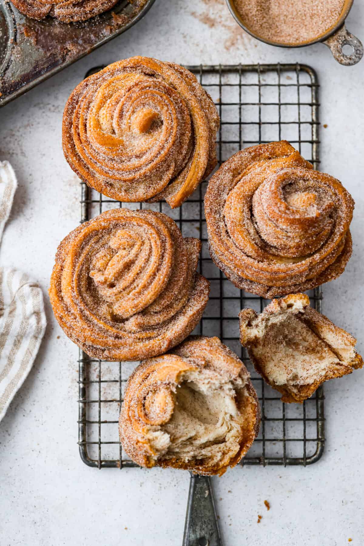 Outrageously wonderful Cruffins are made with just 4 ingredients for a sweet brunch treat that is loved by all! These tender, buttery pastries are made with crescent roll dough rolled up with a cinnamon-sugar mixture and baked until they're fluffy and soft! 5 cruffins on a wire rack. One is torn in half.
