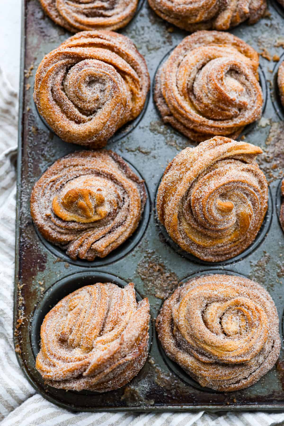 Outrageously wonderful Cruffins are made with just 4 ingredients for a sweet brunch treat that is loved by all! These tender, buttery pastries are made with crescent roll dough rolled up with a cinnamon-sugar mixture and baked until they're fluffy and soft! Baked cruffins in a muffin tin.