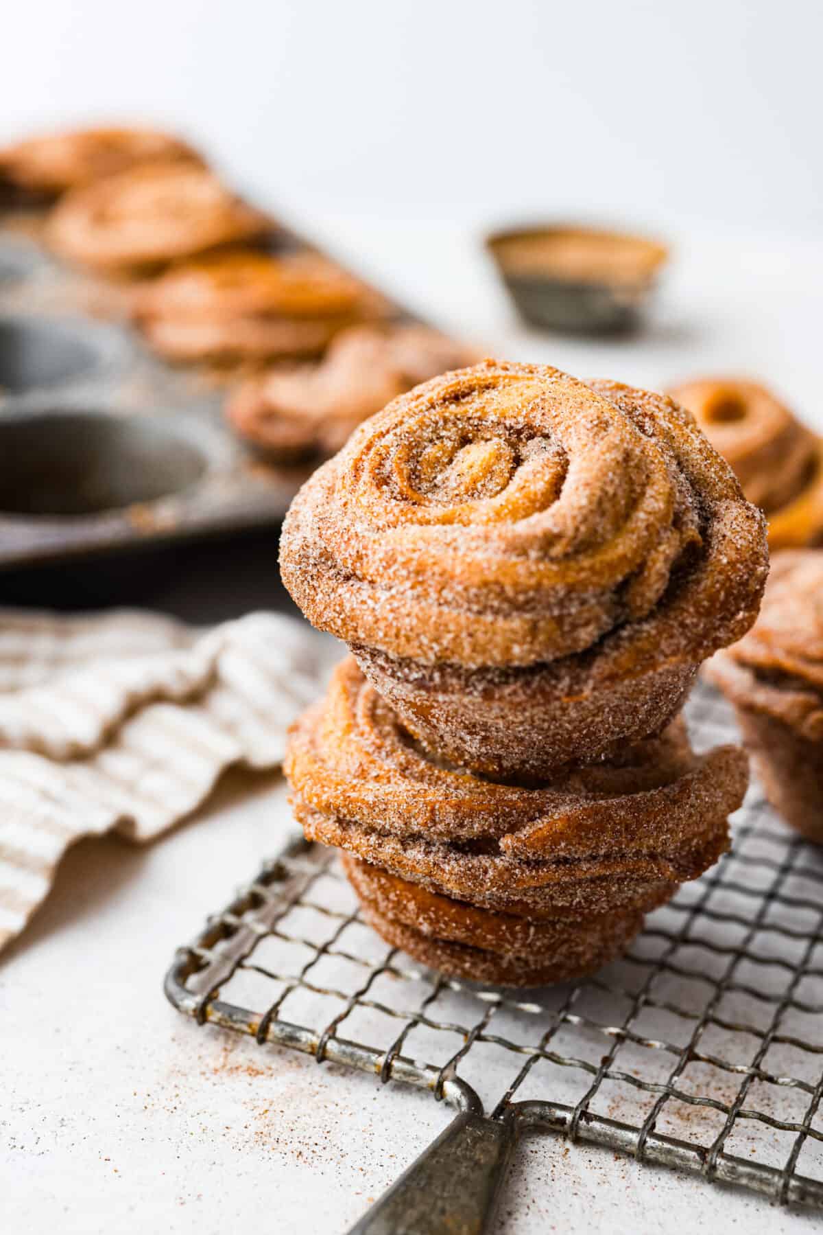 Outrageously wonderful Cruffins are made with just 4 ingredients for a sweet brunch treat that is loved by all! These tender, buttery pastries are made with crescent roll dough rolled up with a cinnamon-sugar mixture and baked until they're fluffy and soft! 2 cruffins stacked on top of each other on a wire rack.