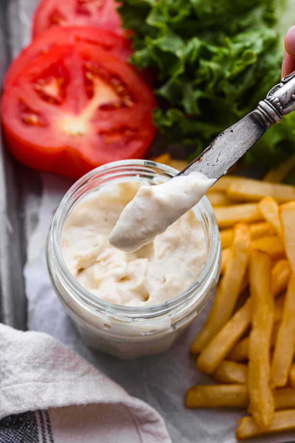 Slather this creamy donkey sauce on your next burger, or serve it with a side of fries! The roasted garlic in this flavor-packed condiment takes this sauce to the next level! Guy Fiery knew how to create a burger sauce the world can't live without! Close top view of a knife lifting donkey sauce from the jar. Fries and burger ingredients are scattered around the jar.