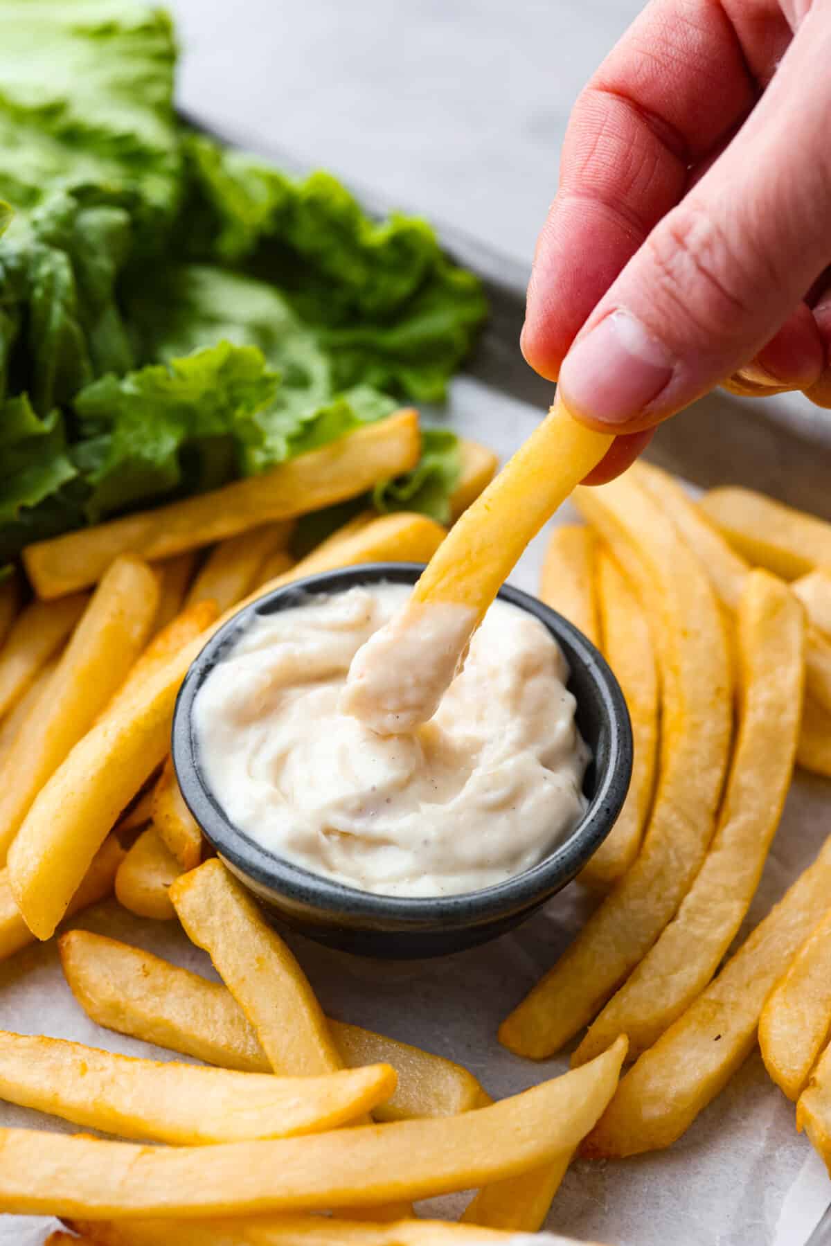 Slather this creamy donkey sauce on your next burger, or serve it with a side of fries! The roasted garlic in this flavor-packed condiment takes this sauce to the next level! Guy Fiery knew how to create a burger sauce the world can't live without! Close view of a French fry dipping in a bowl of donkey sauce. French fries and burger ingredients are scattered around the jar.