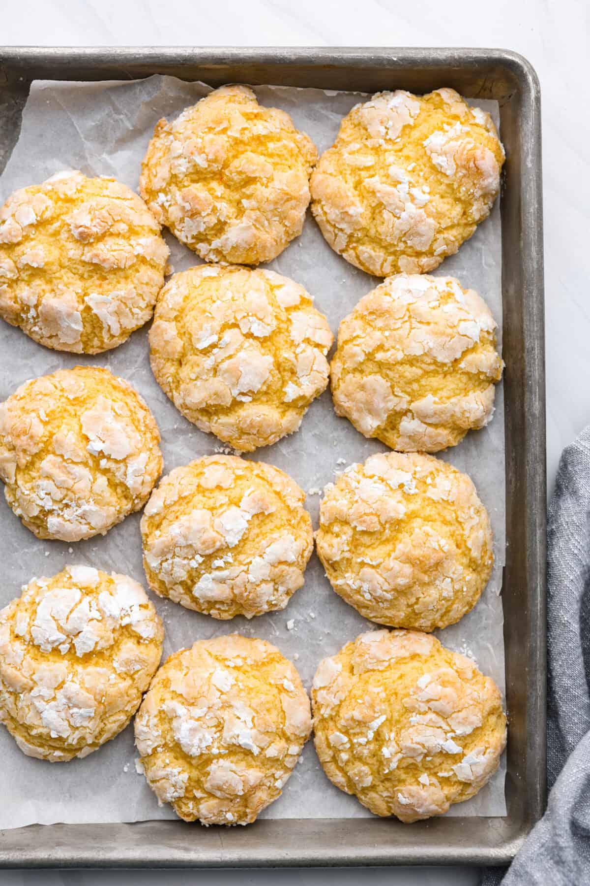 Rich, chewy, and topped with a dusting of powdered sugar, these gooey butter cookies are every cookie lover’s dream! You only need a handful of simple ingredients to make them. Give them a try and watch them fly off the table! Top-down view of gooey butter cookies on a cookie sheet lined with parchment paper.