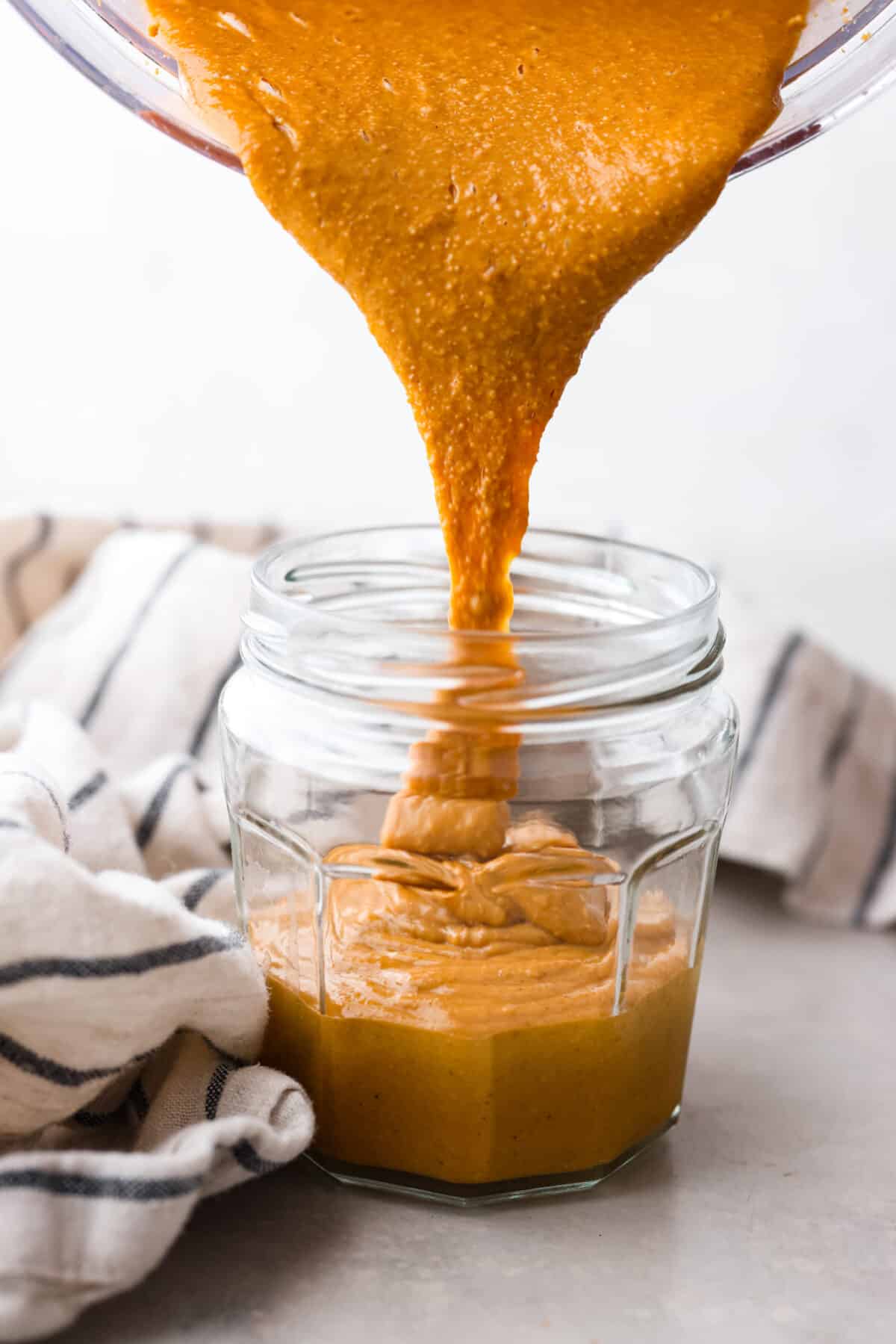 Skip the preservatives and make your own homemade peanut butter in minutes with this easy recipe! So simple and delicious, you won't want it any other way. Pouring peanut butter into a glass jar.