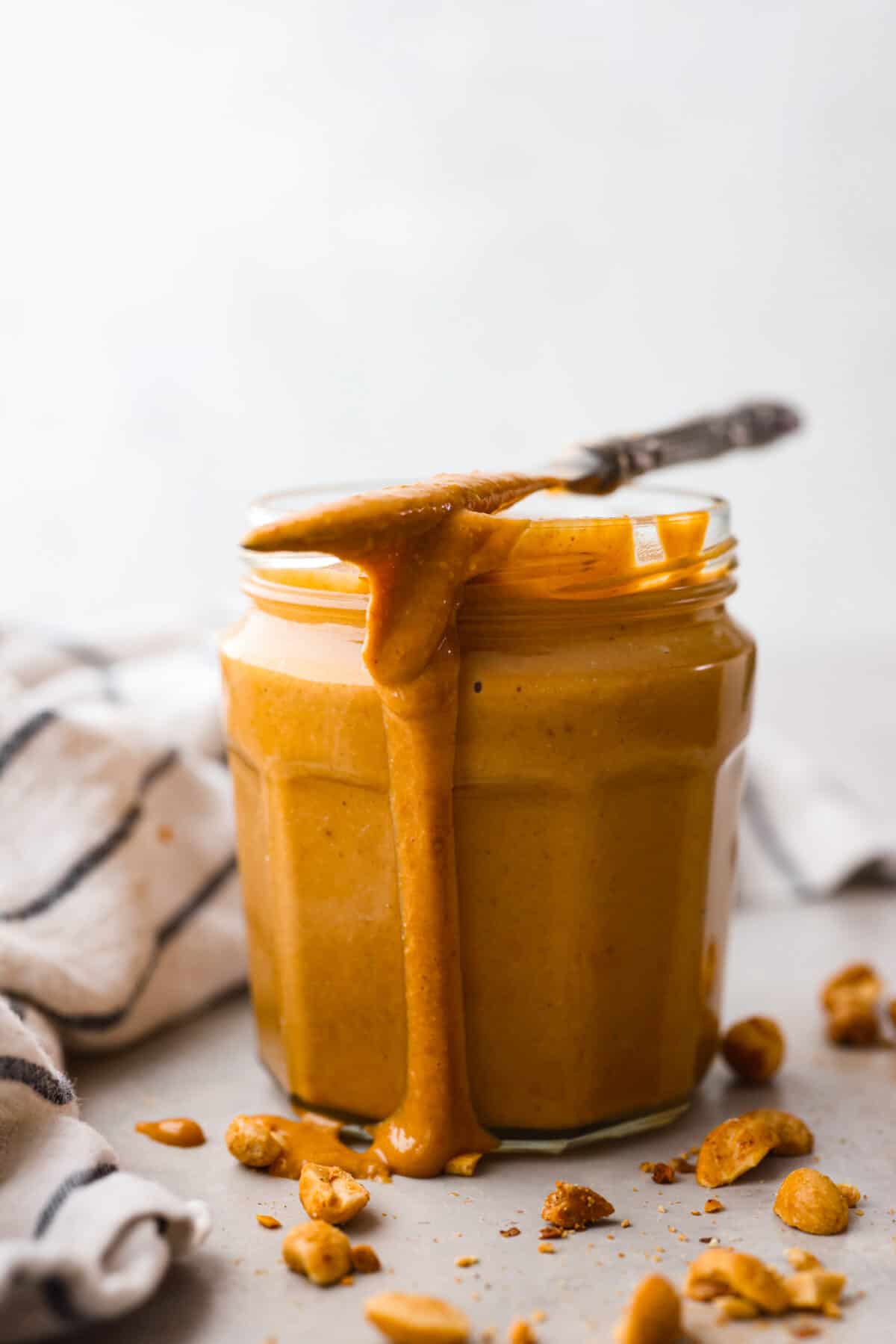 Skip the preservatives and make your own homemade peanut butter in minutes with this easy recipe! So simple and delicious, you won't want it any other way. A glass jar filled with peanut butter, topped with a metal butter knife that also has peanut butter on it.