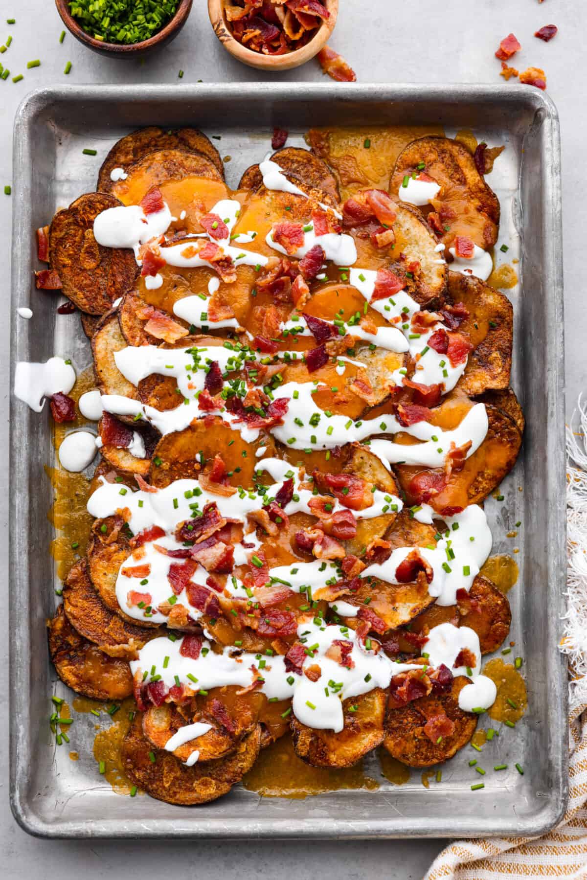 'Irish Nachos' are made with thin russet potato slices, topped with melty cheddar cheese, sour cream, bacon bits, and chives! Toasted to golden perfection, they're sure to be a crowd-pleaser! Top-down view of russet potato slices topped with bacon, chives, and sour cream.