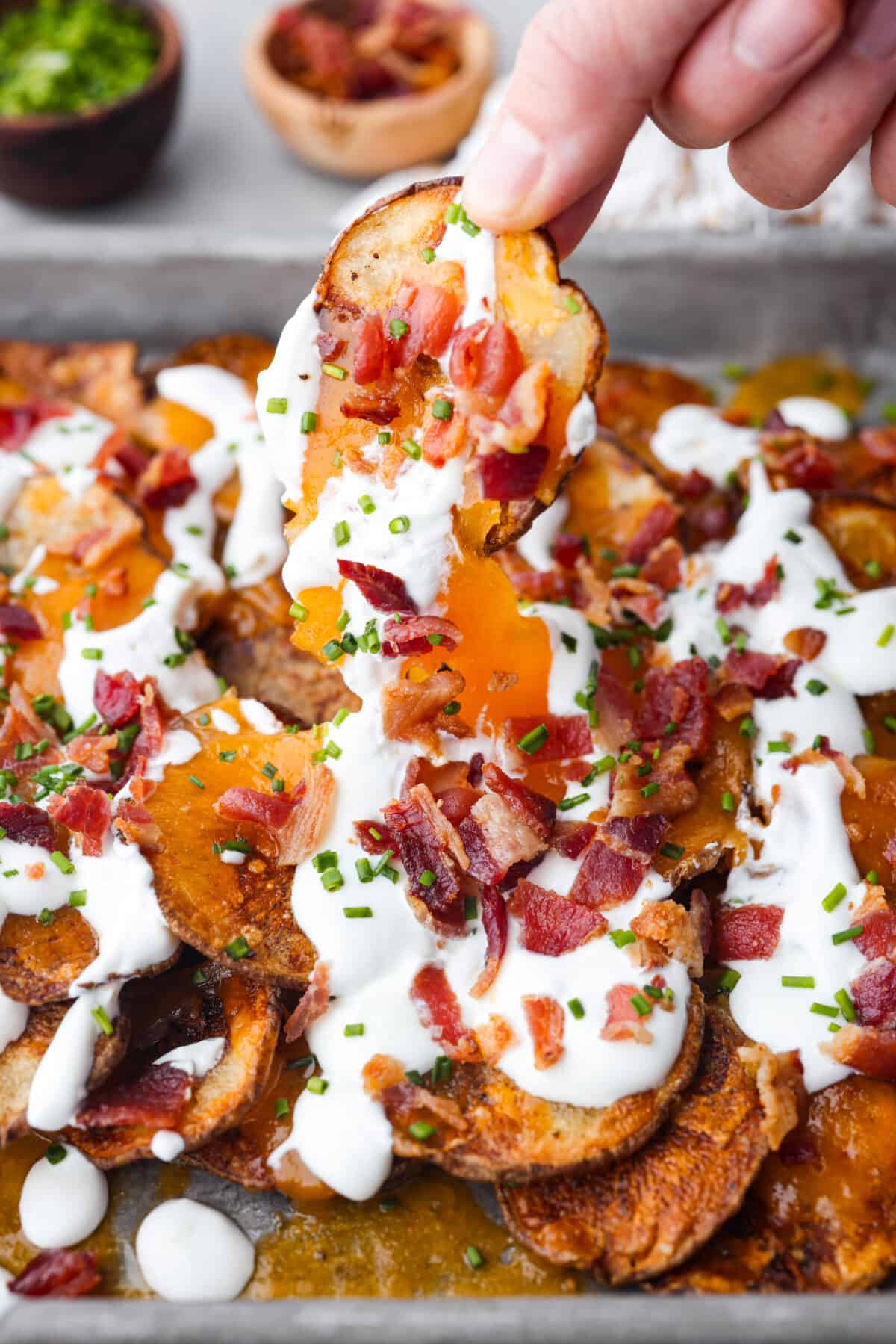 'Irish Nachos' are made with thin russet potato slices, topped with melty cheddar cheese, sour cream, bacon bits, and chives! Toasted to golden perfection, they're sure to be a crowd-pleaser! Picking up an Irish nacho.