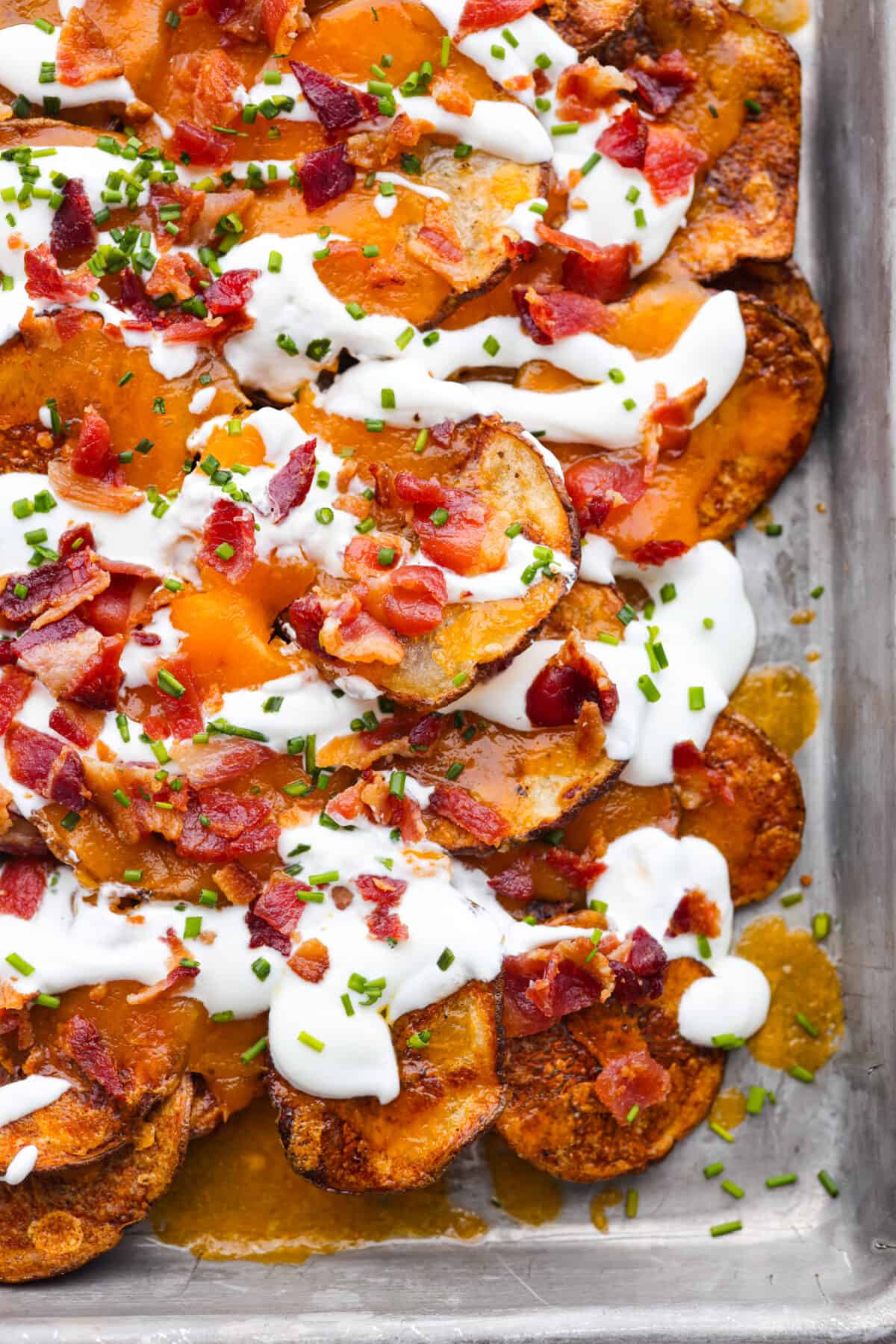 'Irish Nachos' are made with thin russet potato slices, topped with melty cheddar cheese, sour cream, bacon bits, and chives! Toasted to golden perfection, they're sure to be a crowd-pleaser! Closeup of Irish nachos.