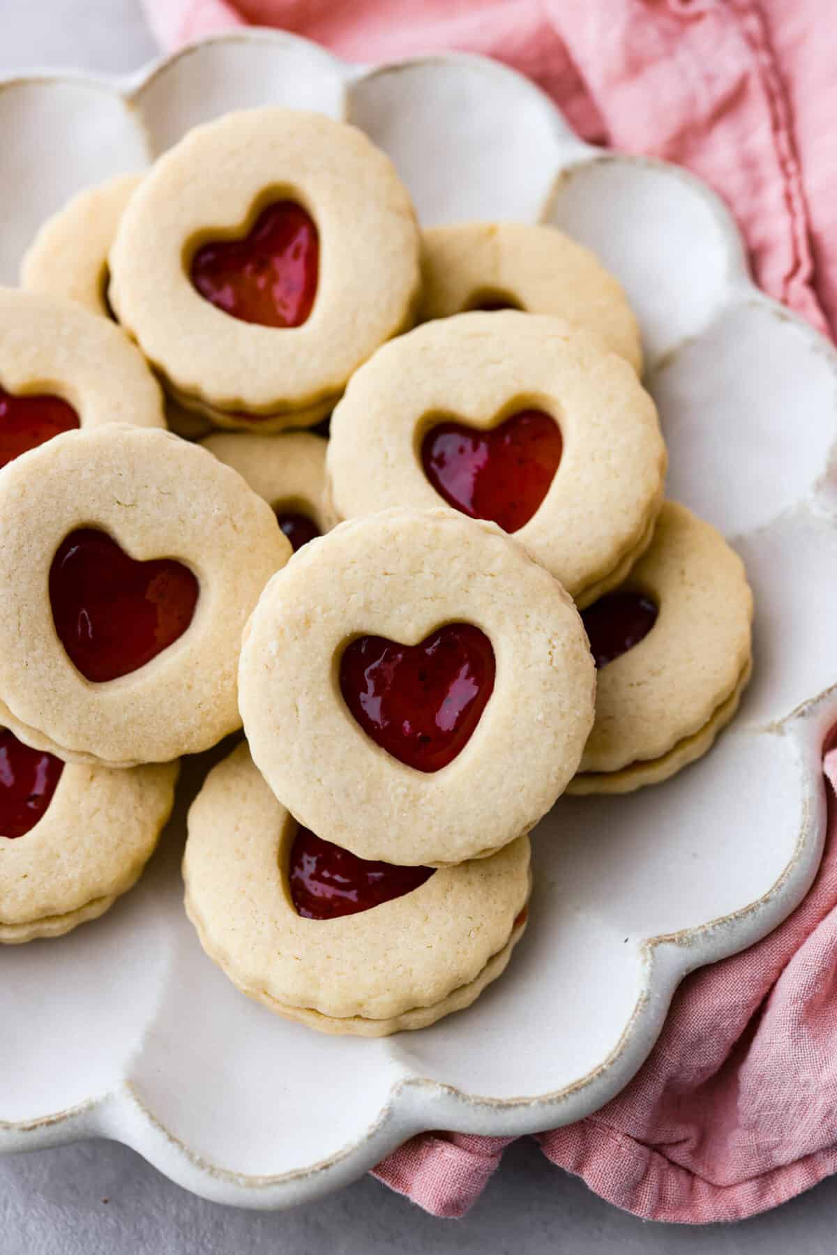 Adorable Jammie Dodgers feature tart strawberry jam sandwiched betweenย buttery shortbread cookies for a gorgeous treat that will be the star of any dessert spread! Cookies served in a white, scalloped dish.