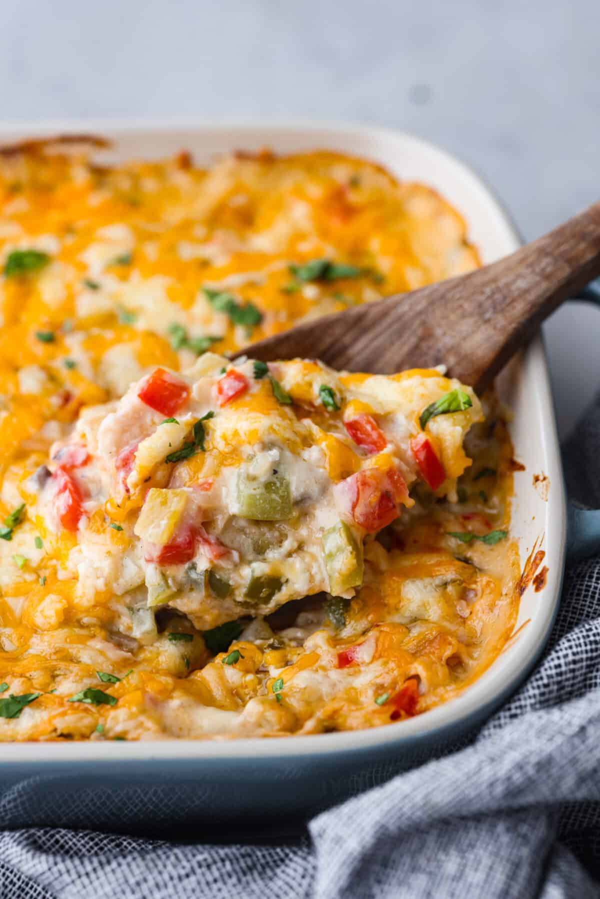 King Ranch Casserole is your solution if you're looking for a dinner that is both delicious and easy to make! It's a creamy dish with layers of chicken, cheese, and tortilla chips that your family is going to want on repeat. Close view of king ranch casserole in a baking dish with a wooden serving spoon.