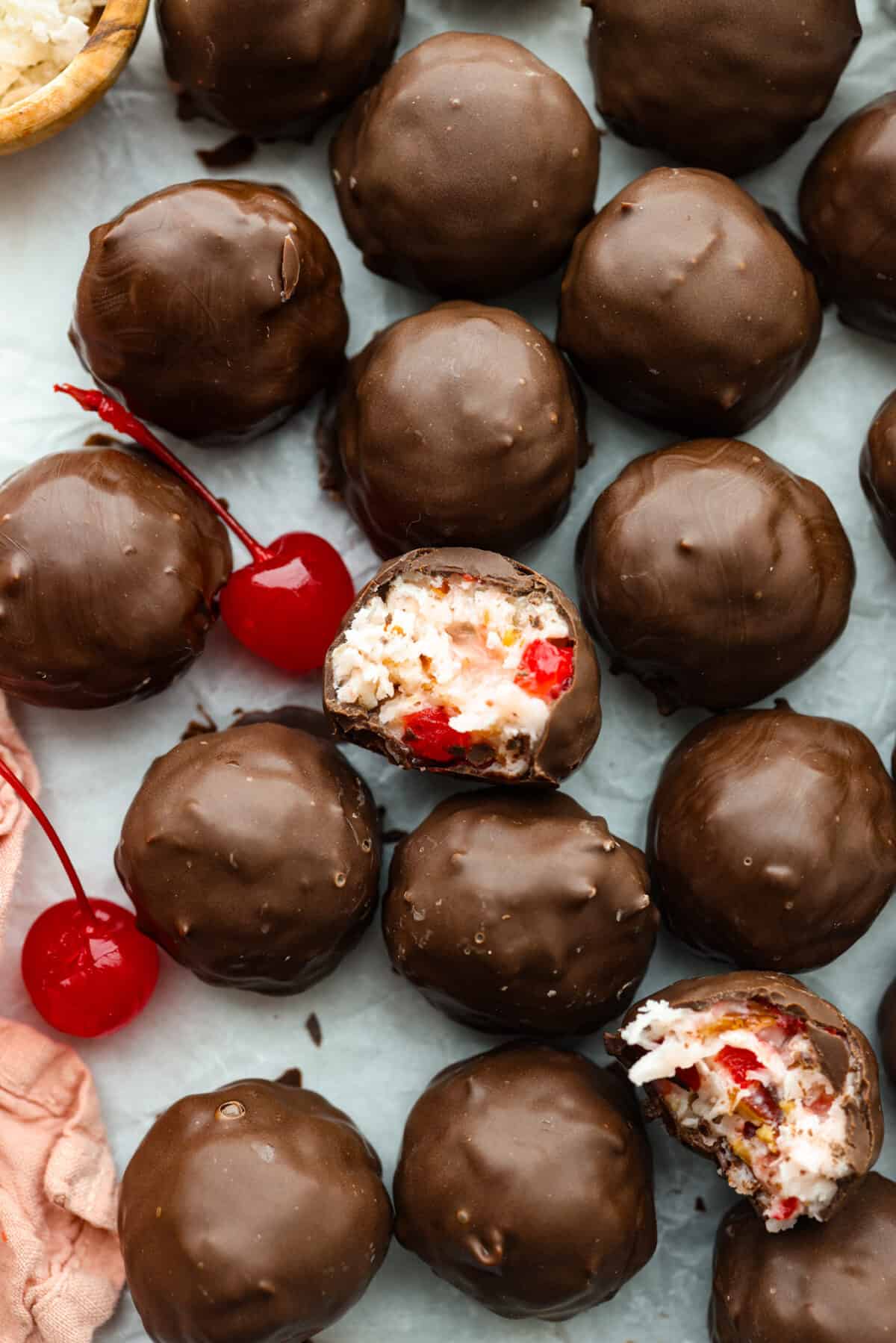 Martha Washington Candy is an easy no-bake treat filled with cherries, coconut and pecans, and then coated in chocolate. Perfect for Christmas and Valentine’s Day! Top-down view of Martha Washington Candy. One truffle is broken in half, you can see its cherry filling.