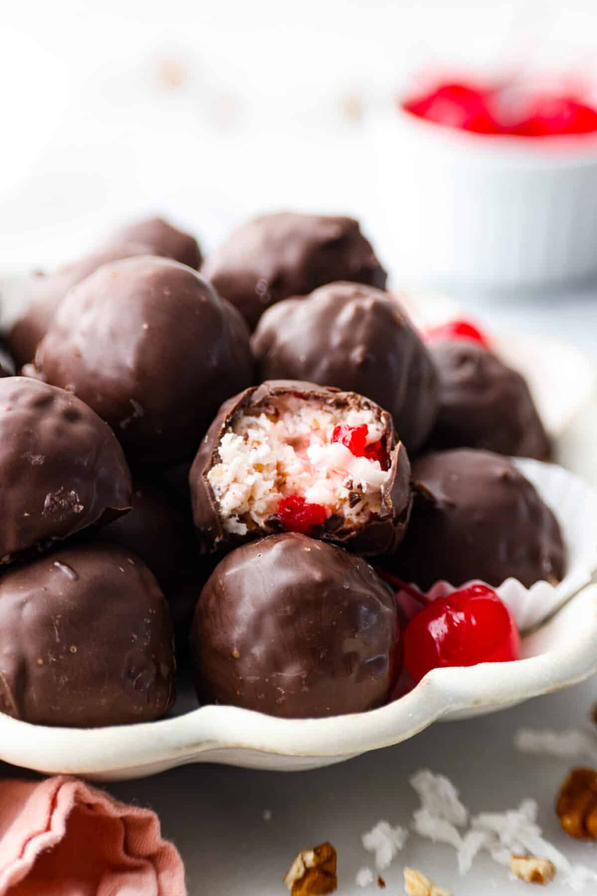 Martha Washington Candy is an easy no-bake treat filled with cherries, coconut and pecans, and then coated in chocolate. Perfect for Christmas and Valentine’s Day! Chocolate-coated cherry truffles in a white scalloped serving dish.