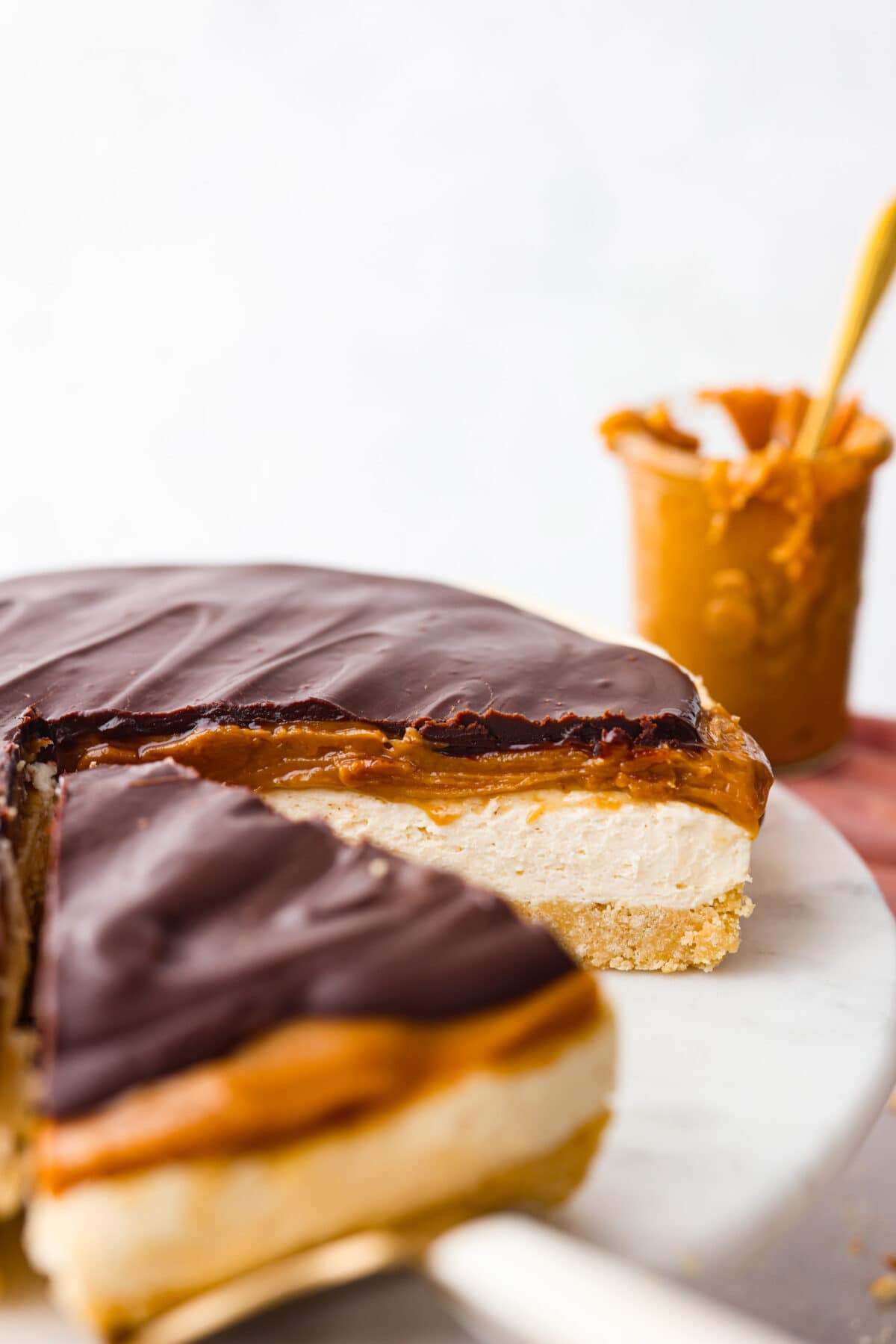 Delight in pure dessert heaven with this No-Bake Millionaire Cheesecake! It has four amazing layers that start with a shortbread crust, topped with a creamy cheesecake filling, then rich caramel and chocolate ganache to finish it off. And the best part? Itโs so easy to make with no baking required! A full millionaire cheesecake with a slice taken out of it.