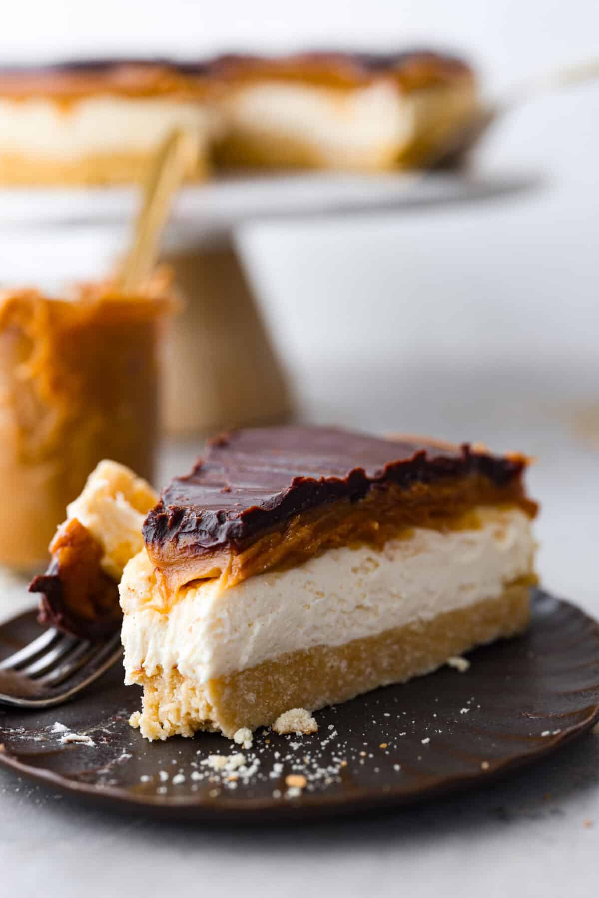 Delight in pure dessert heaven with this No-Bake Millionaire Cheesecake! It has four amazing layers that start with a shortbread crust, topped with a creamy cheesecake filling, then rich caramel and chocolate ganache to finish it off. And the best part? Itโs so easy to make with no baking required! A slice of millionaire cheesecake.