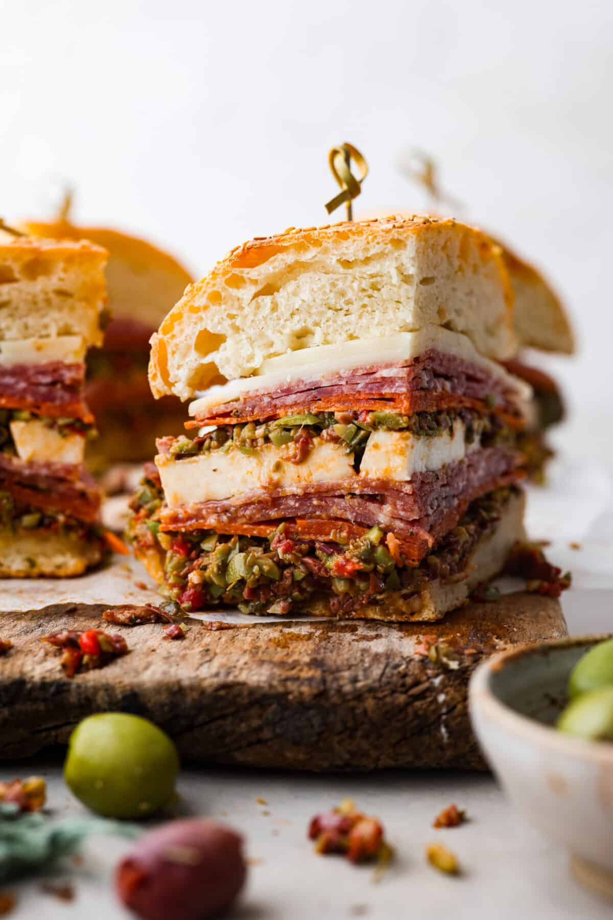 The Muffuletta is an iconic sandwich from New Orleans that is piled high with layers of meat, cheese and a delicious olive salad! Served on either Italian bread or muffuletta bread, youโll be obsessed after the first bite! A quarter of a muffuletta sandwich, held together with a toothpick.