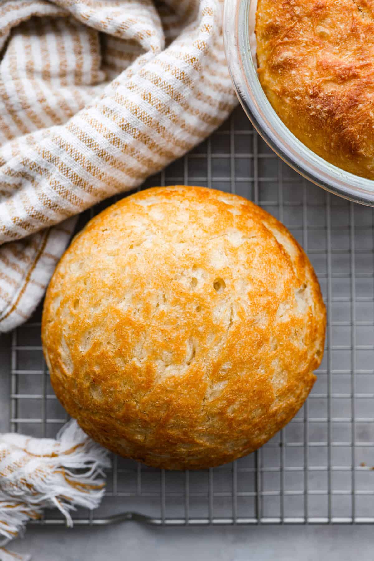 Make soft homemade bread without any kneading! This easy peasant bread recipe only uses 6 ingredients to make two perfect loaves of bread. Fluffy on the inside with a buttery golden crust on the outside. Top view of a loaf of peasant bread on a cooling rack.