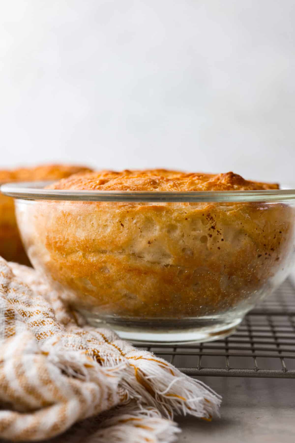 Make soft homemade bread without any kneading! This easy peasant bread recipe only uses 6 ingredients to make two perfect loaves of bread. Fluffy on the inside with a buttery golden crust on the outside. Close side view of the peasant bread baked in a glass bowl.