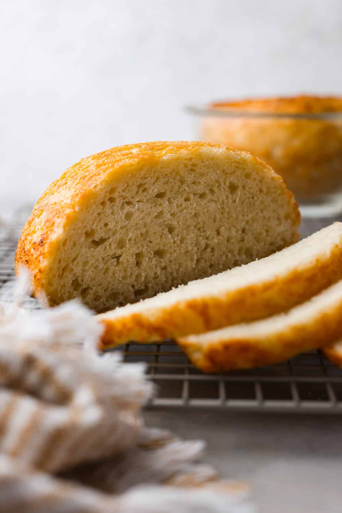 Make soft homemade bread without any kneading! This easy peasant bread recipe only uses 6 ingredients to make two perfect loaves of bread. Fluffy on the inside with a buttery golden crust on the outside. Close side view of sliced peasant bread on a cooling rack.