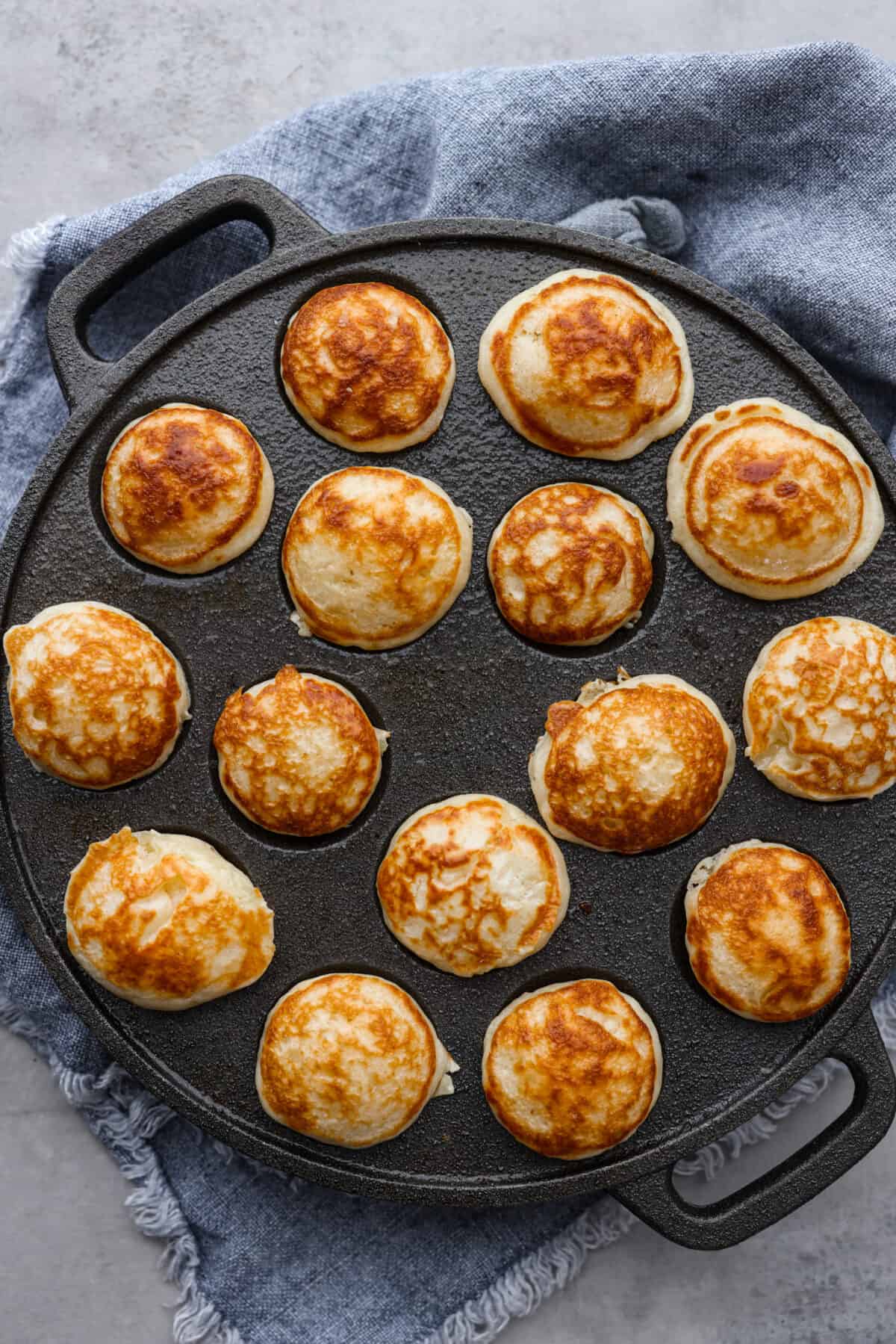 Poffertjes are small, fluffy Dutch pancakes that are so delicious for breakfast! Serve them with a dusting of powdered sugar and fresh berries for a meal that everyone will love. Top-down view of cooked poffertjes in a pan.