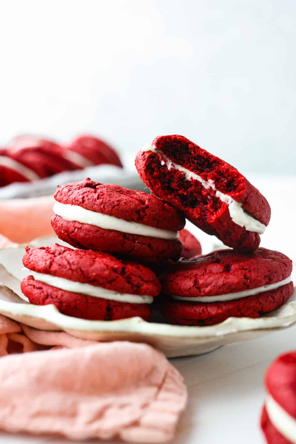 These vibrant red velvet Oreos are filled with a sweet cream cheese frosting and are irresistibly cute! Super easy to make from a red velvet cake mix, but SO delicious that no one will ever know. Close view of red velvet Oreos on a plate with a bite out of one of the cookies.