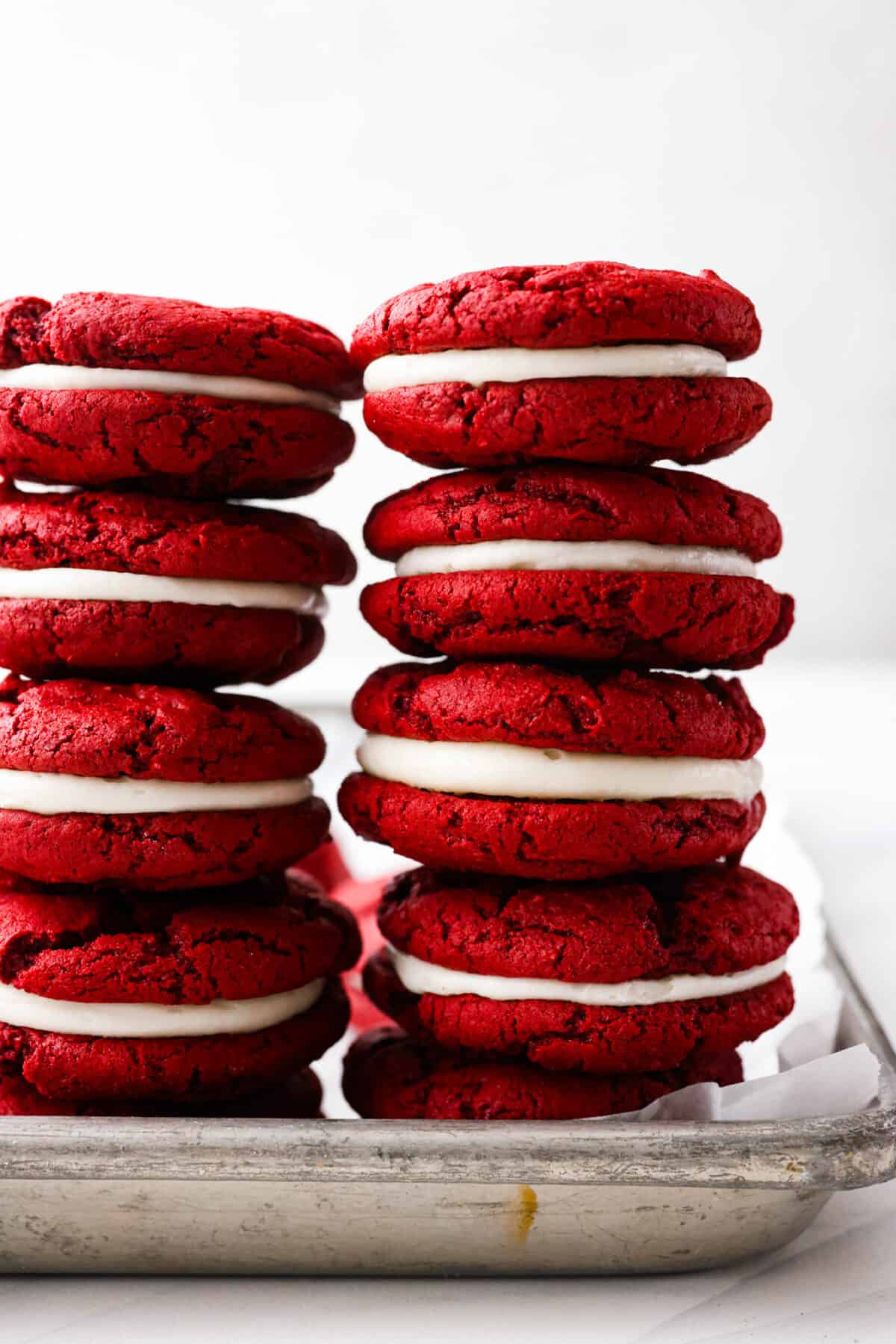 These vibrant red velvet Oreos are filled with a sweet cream cheese frosting and are irresistibly cute! Super easy to make from a red velvet cake mix, but SO delicious that no one will ever know. Close view of red velvet Oreos stacked.