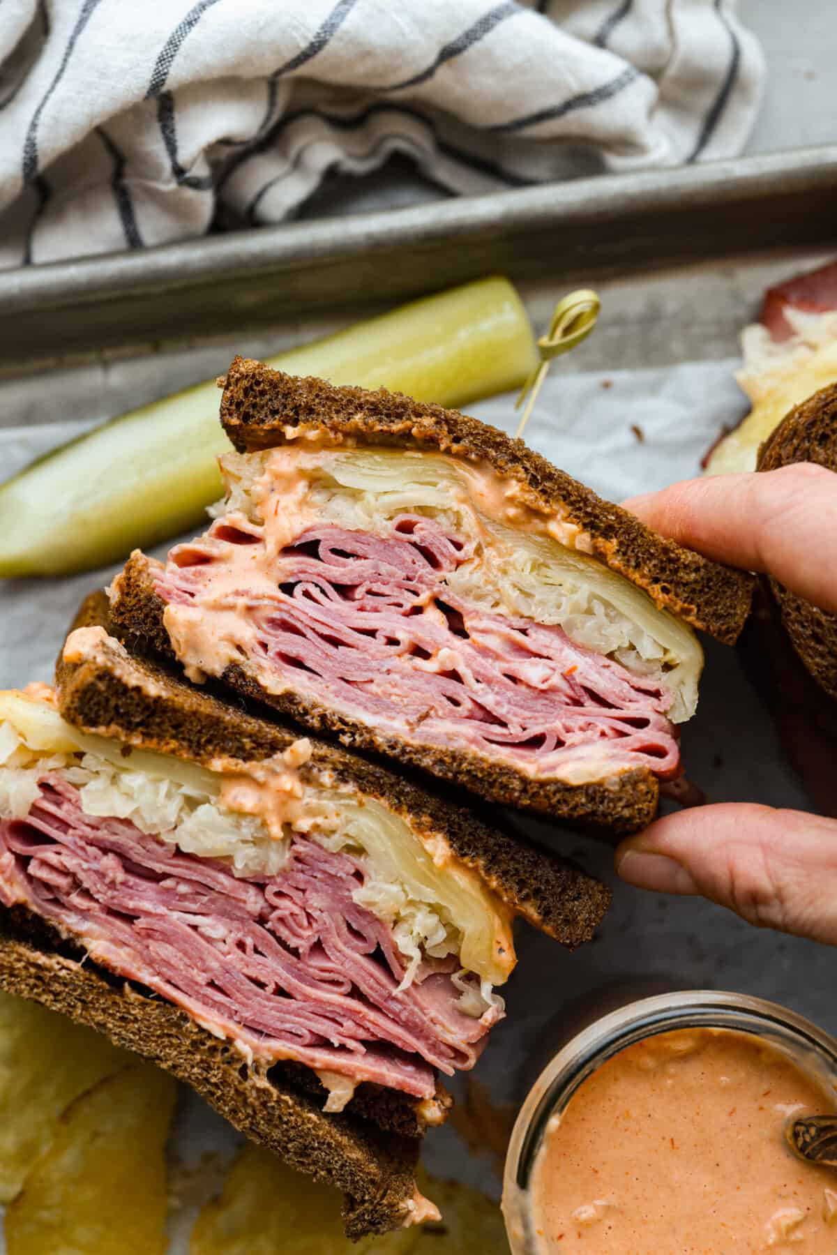 This incredible Reuben Sandwich is stuffed to the brim on rye bread with layers of thinly sliced corned beef, plenty of Swiss cheese, sauerkraut, and dressing. Broiled until the cheese is melty and everything is warm and flavorful, this is one epic sandwich! A sandwich cut in half, so the corned beef, sauerkraut, and swiss cheese filling can be seen.