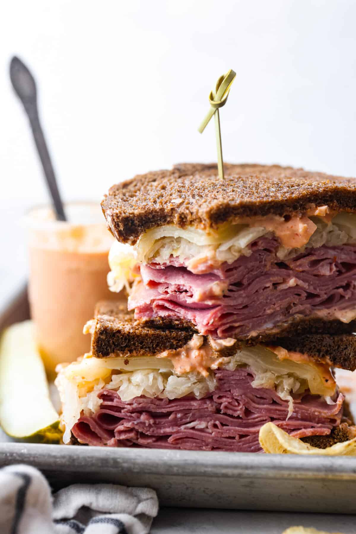 This incredible Reuben Sandwich is stuffed to the brim on rye bread with layers of thinly sliced corned beef, plenty of Swiss cheese, sauerkraut, and dressing. Broiled until the cheese is melty and everything is warm and flavorful, this is one epic sandwich! 2 sandwich halves stacked on top of each other. One has a bite taken out of it.