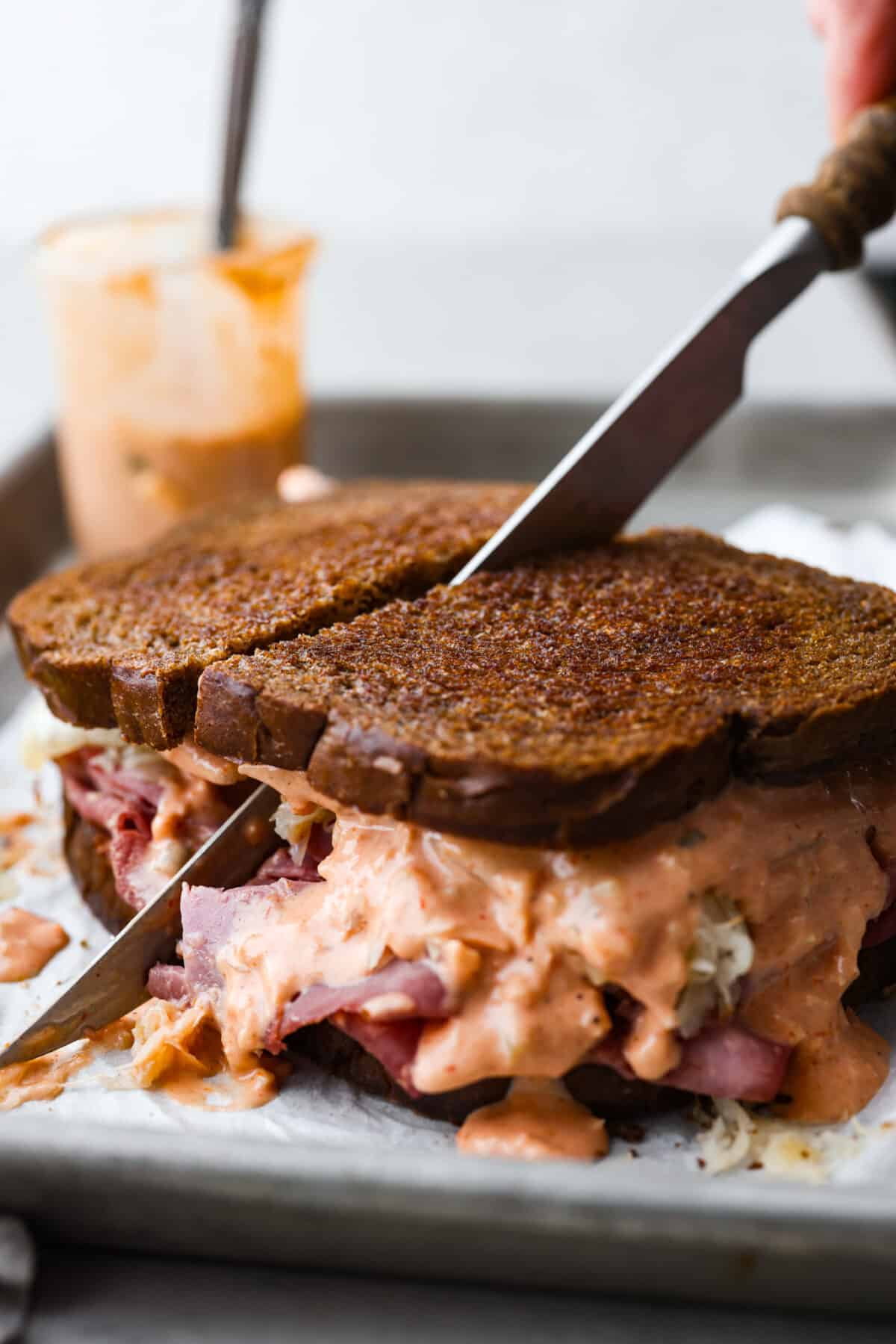 Homemade Russian dressing is a creamy and flavorful condiment perfect for sandwiches, burgers, and even as a dip. It's easy to make with simple ingredients and has the perfect balance of sweet, tangy, and spicy flavors. Cutting a sandwich made with Russian dressing in half.
