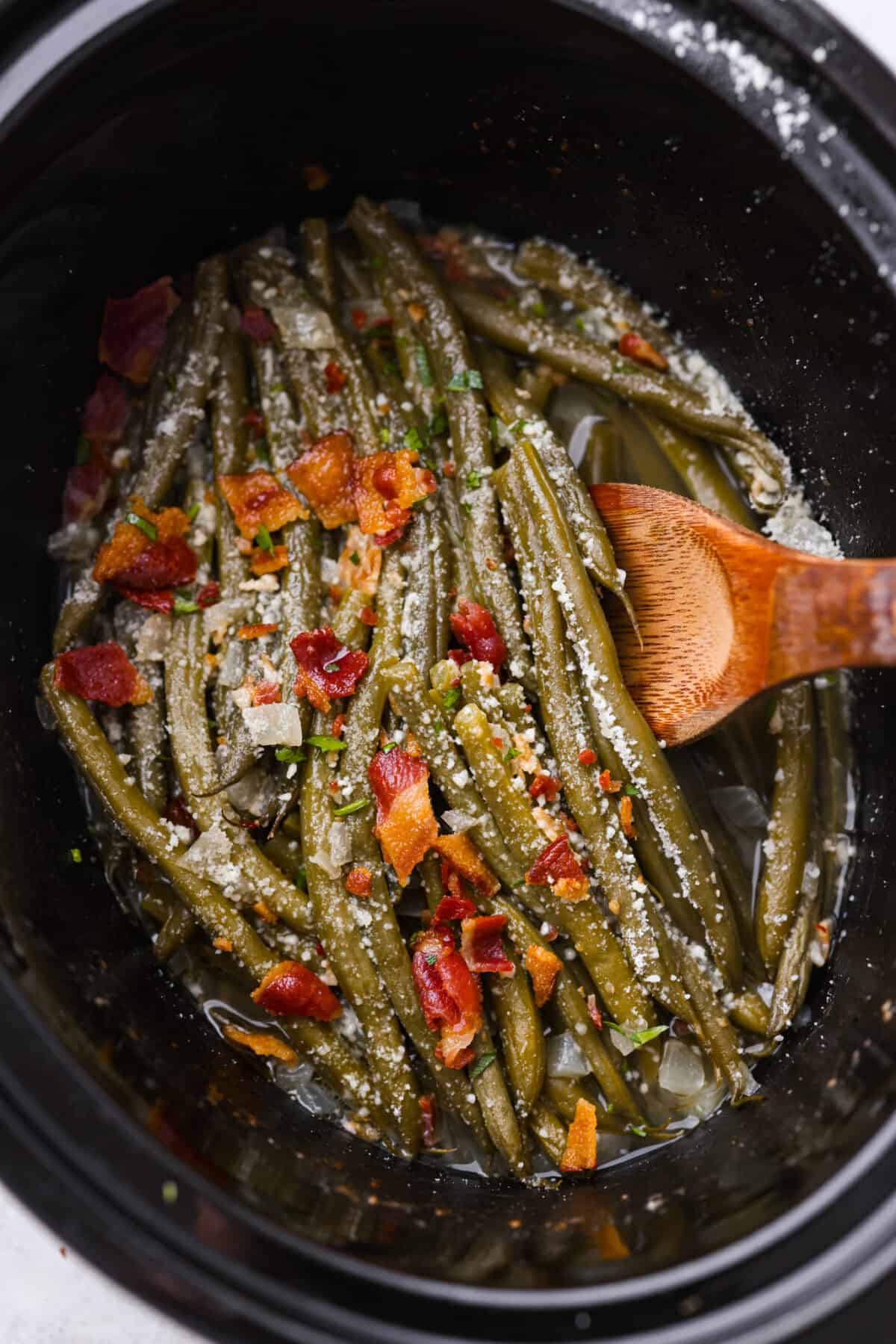 These Crockpot Green Beans are perfectly tender, packed with flavor and so easy to cook in your slow cooker. All you need is 5 minutes of prep time to have a side dish that pairs well with almost any meal! Green beans in a slow cooker, topped with cheese and bacon.