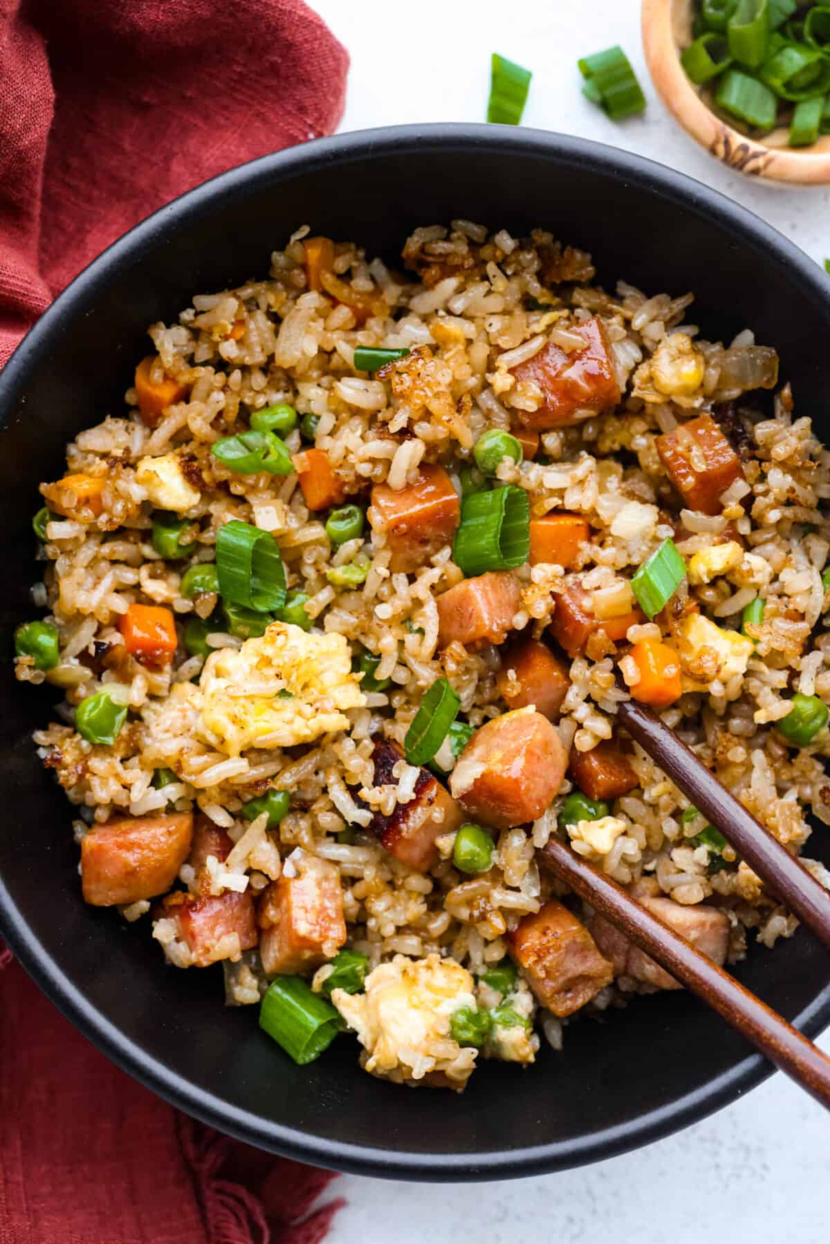 This combination of salty, pan-fried spam, fluffy rice, eggs, and veggies will have you hooked. With how delicious and easy-to-make spam fried rice is, be prepared for it to be a regular in your dinner rotation! A serving of fried rice in a black bowl.