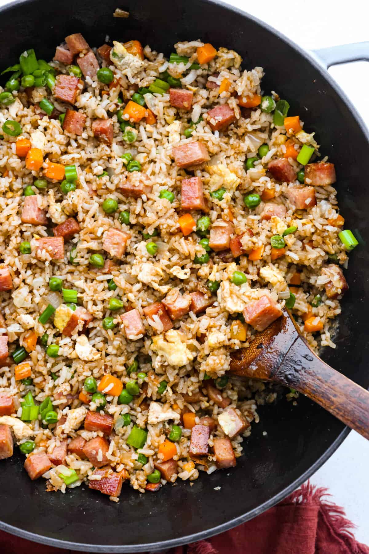 This combination of salty, pan-fried spam, fluffy rice, eggs, and veggies will have you hooked. With how delicious and easy-to-make spam fried rice is, be prepared for it to be a regular in your dinner rotation! Spam fried rice in a wok, being stirred with a wooden spoon.