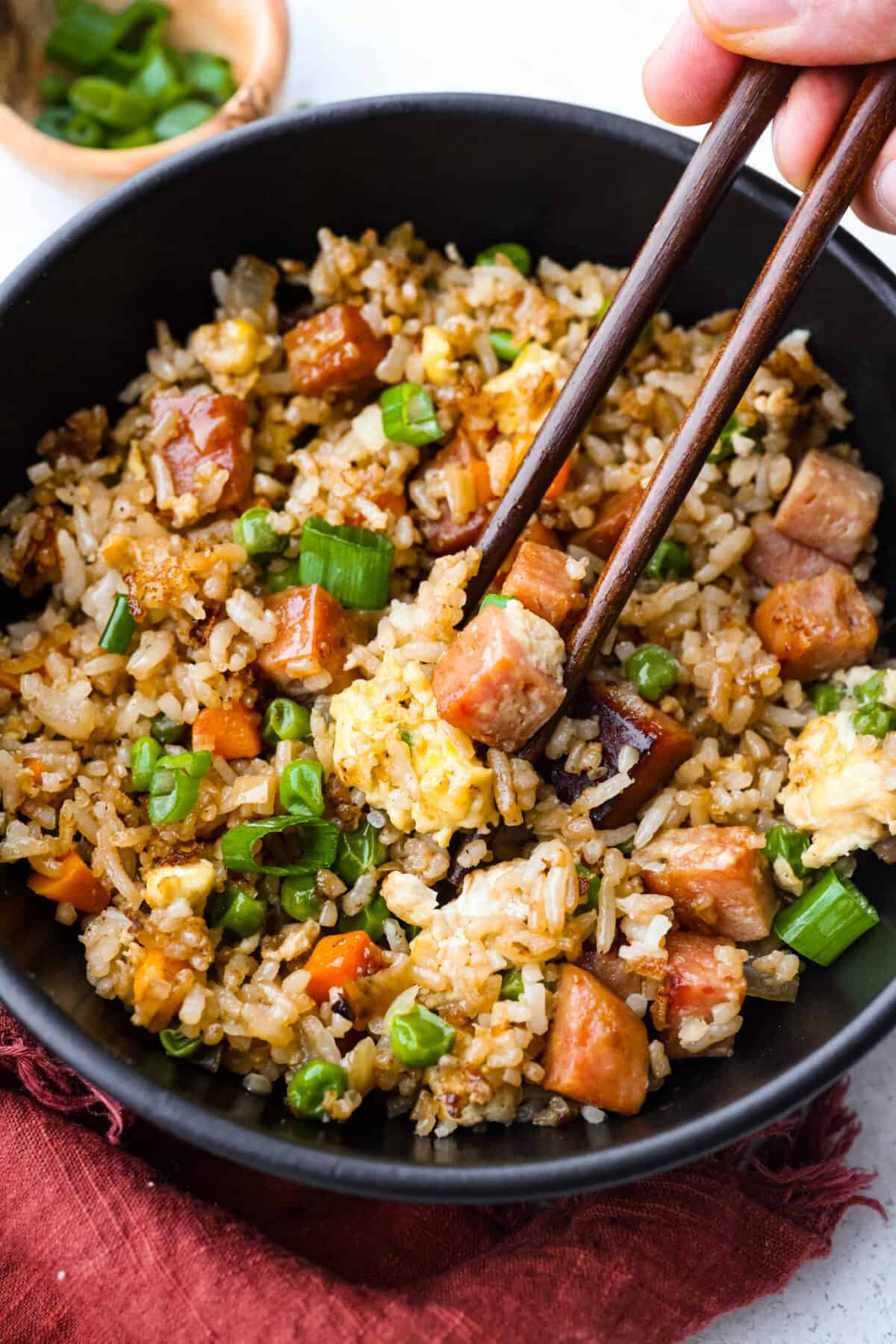 This combination of salty, pan-fried spam, fluffy rice, eggs, and veggies will have you hooked. With how delicious and easy-to-make spam fried rice is, be prepared for it to be a regular in your dinner rotation! Picking up a piece of cubed spam with chopsticks.