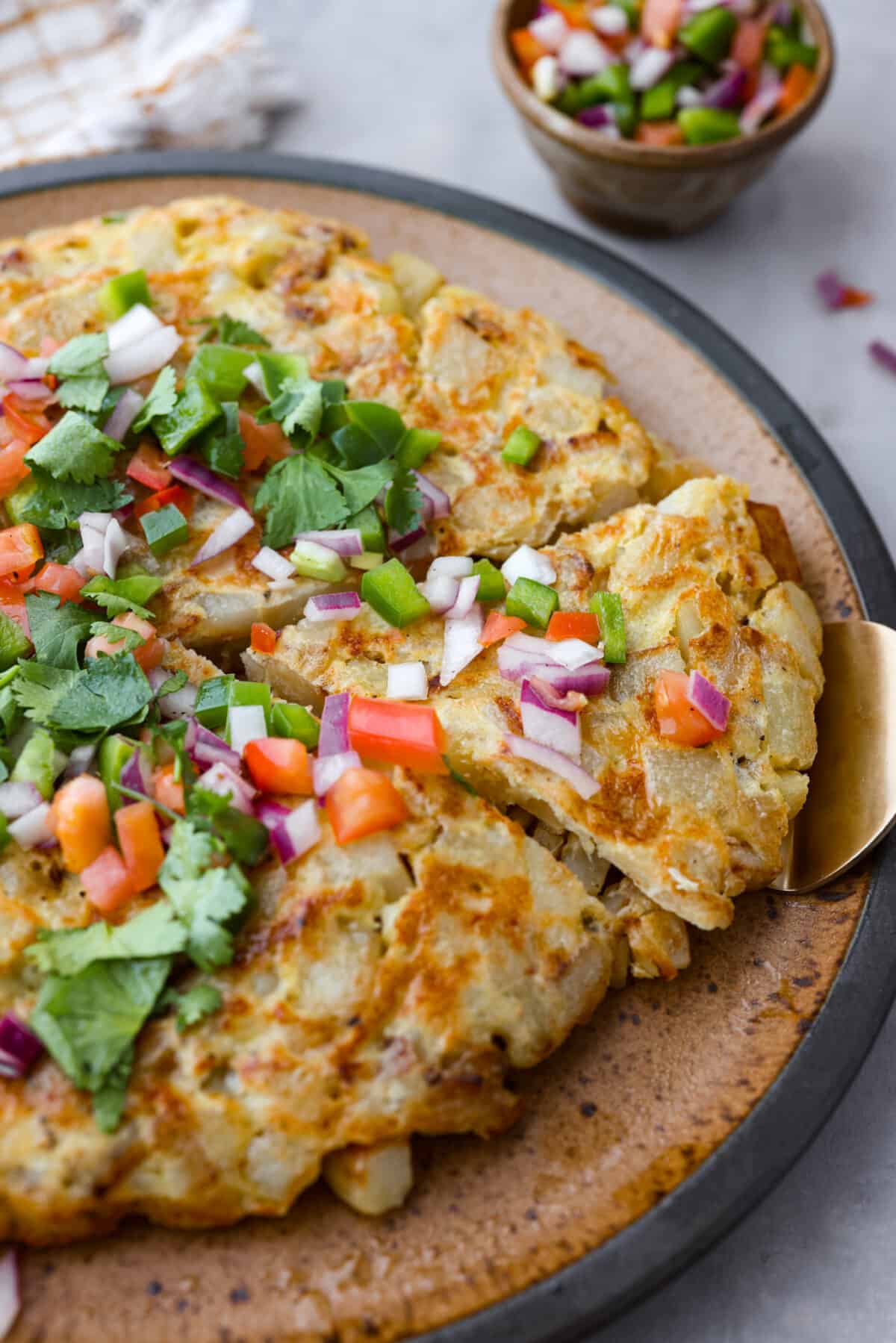 Make this delicious traditional Spanish tortilla at home! Tender potatoes, eggs, and onions cooked together in a skillet and topped with fresh salsa. Bring the flavors of Spain to your kitchen! Close view of Spanish tortilla on a large plate garnished with salsa and cilantro.