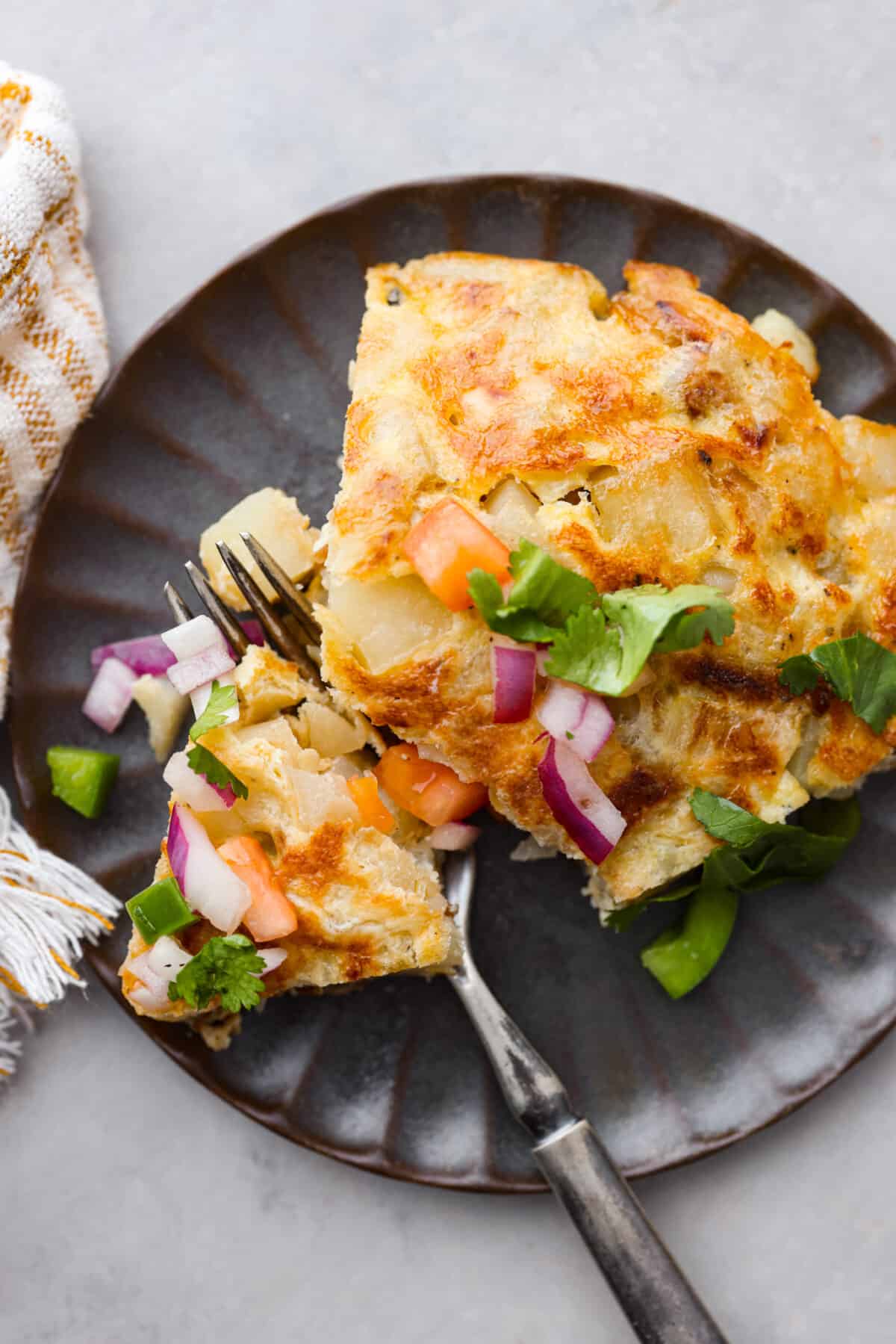 Make this delicious traditional Spanish tortilla at home! Tender potatoes, eggs, and onions cooked together in a skillet and topped with fresh salsa. Bring the flavors of Spain to your kitchen! Close view of a slice or Spanish tortilla on a small plate with a fork.