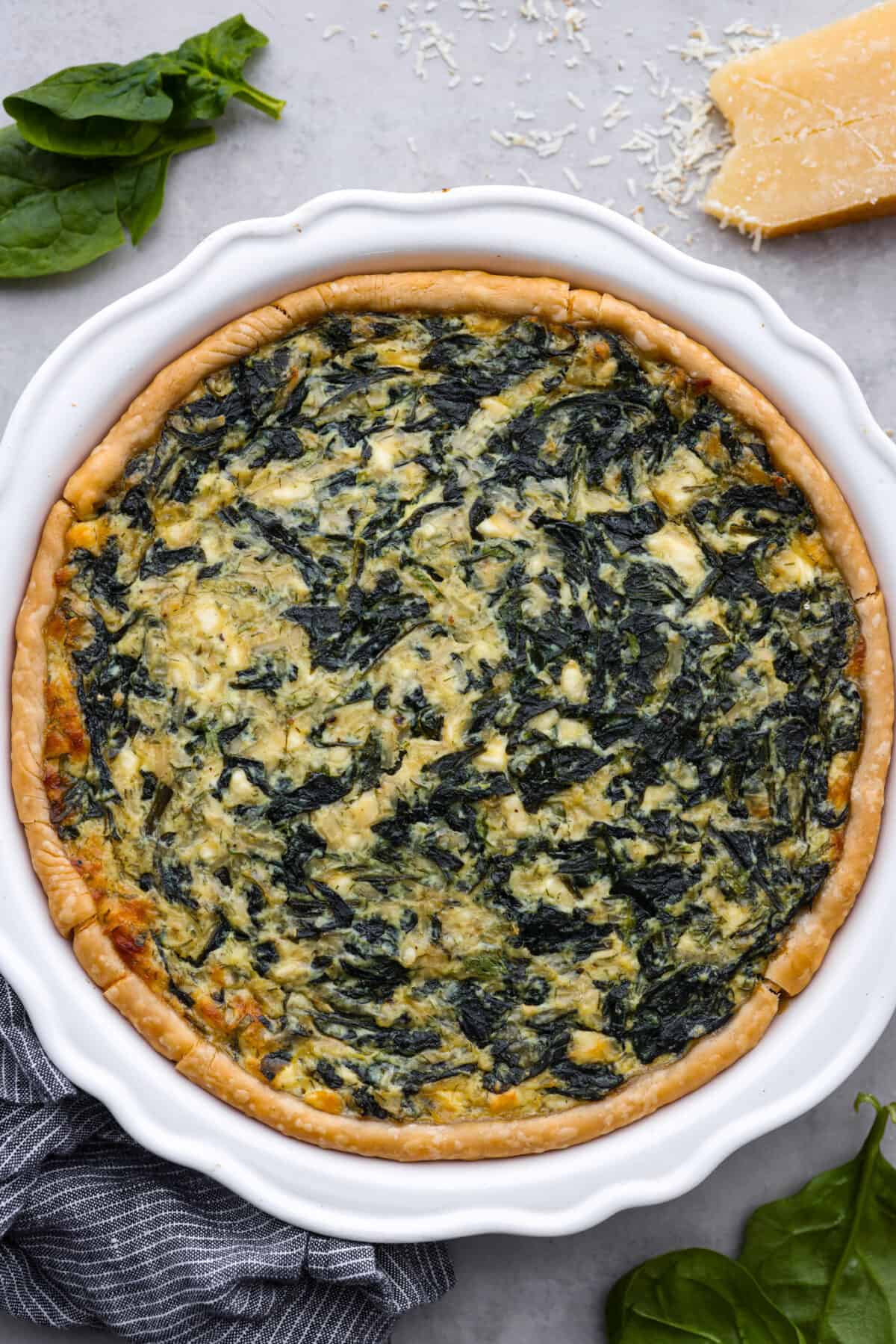 This savory spinach pie is packed with spinach and baked in a flaky crust. It's loaded with three kinds of cheeses, onion, garlic, eggs, and seasoned with tons of flavor! Enjoy it warm or cold, and any time of day. Top view of the baked spinach pie in a white pie dish.