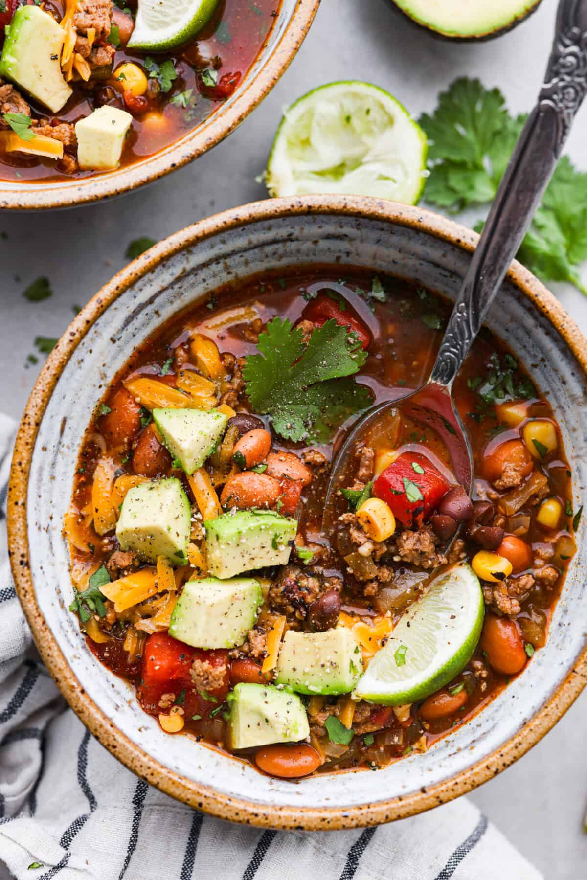 This one-pot taco soup delivers all the bold, Tex-Mex goodness you love with simple pantry staples and minimal prep! Plus, it's ready to go in 30 minutes. This is one of my family’s favorite dinners and I know you’ll love it just as much. A bowl of taco soup, topped with chopped avocado, shredded cheese, cilantro, and a lime wedge.
