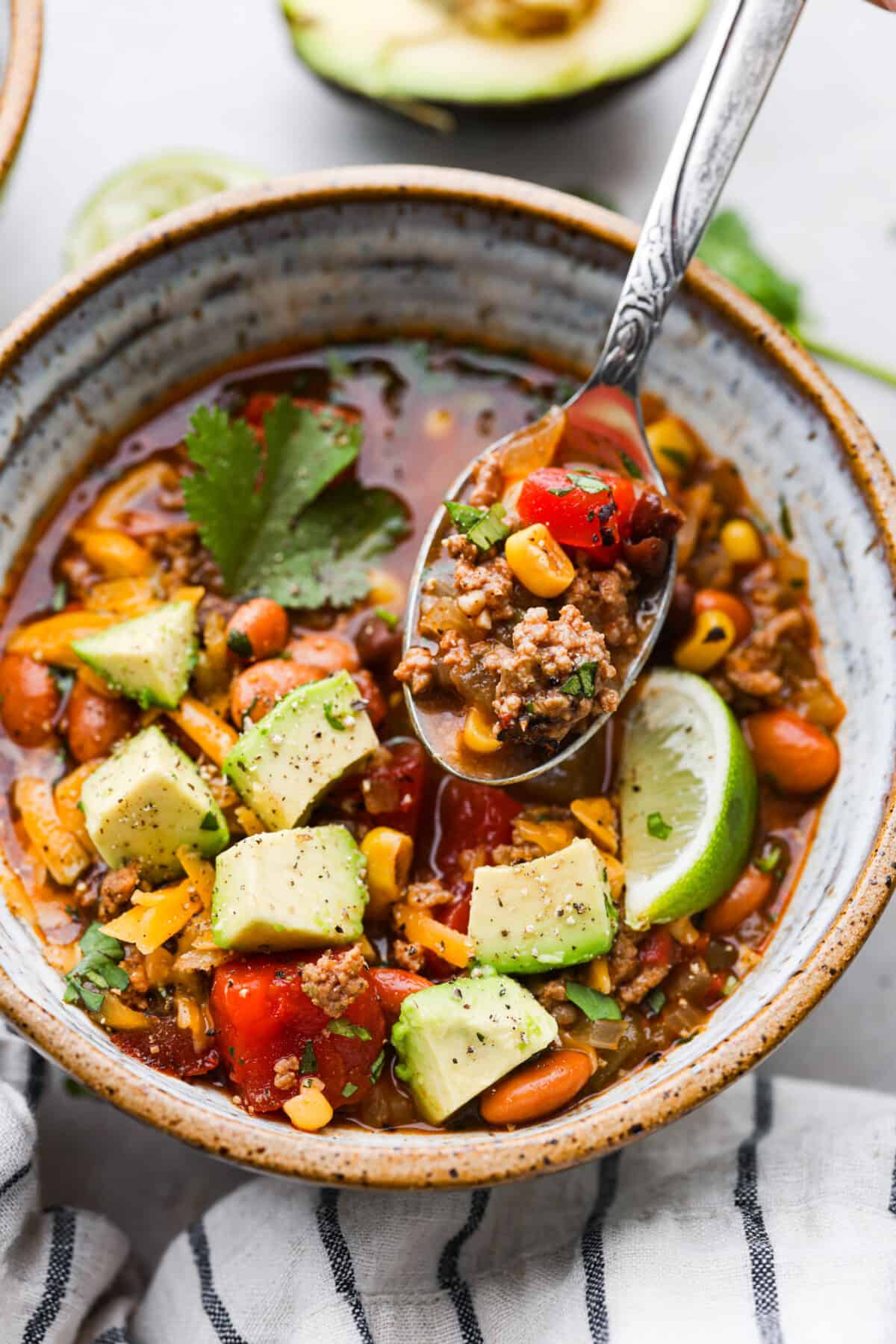 This one-pot taco soup delivers all the bold, Tex-Mex goodness you love with simple pantry staples and minimal prep! Plus, it's ready to go in 30 minutes. This is one of my family’s favorite dinners and I know you’ll love it just as much. Closeup of a serving of taco soup, with ground beef, broth, and vegetables in a metal spoon.
