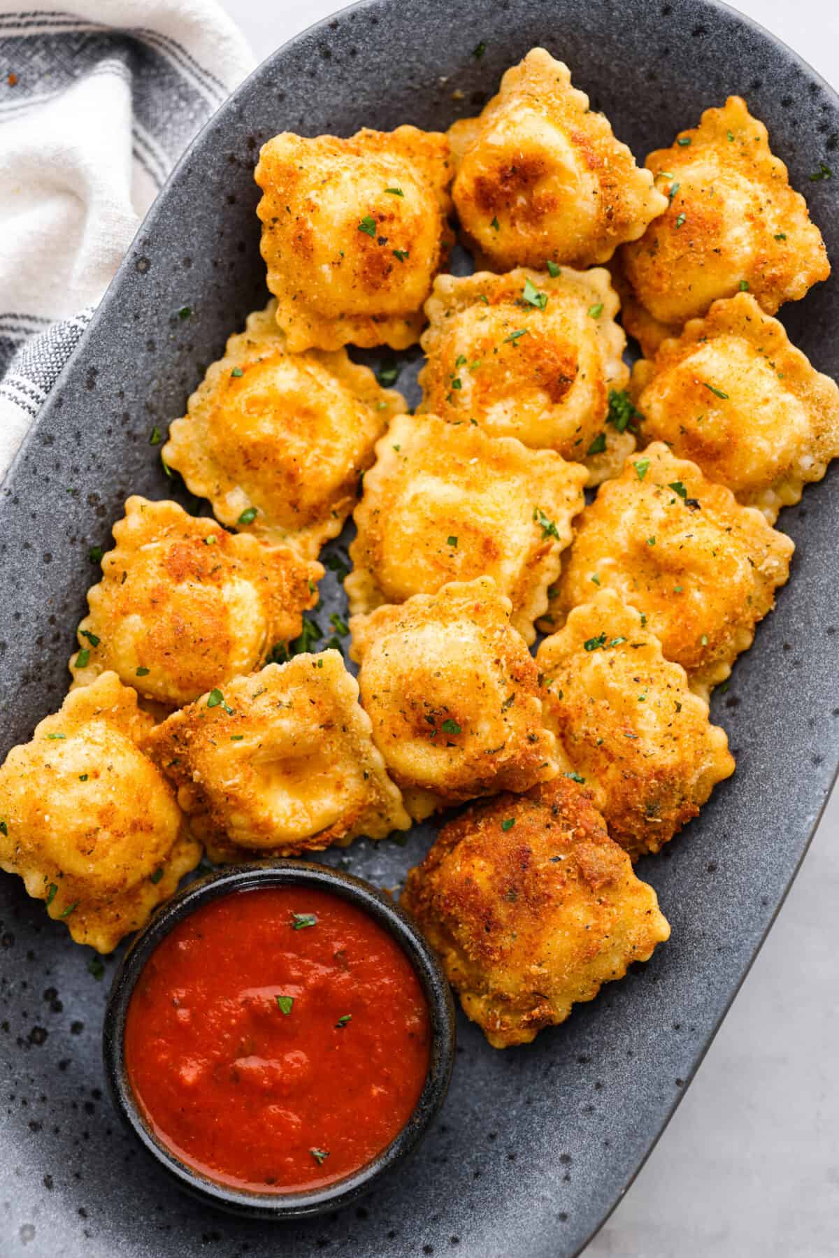 Tender ravioli coated in Italian breadcrumbs and parmesan cheese, toasted to golden brown perfection! Served with a side of marinara for dipping, this is one appetizer you donโt want to miss! Toasted ravioli on a gray serving platter, with a side of marinara sauce.