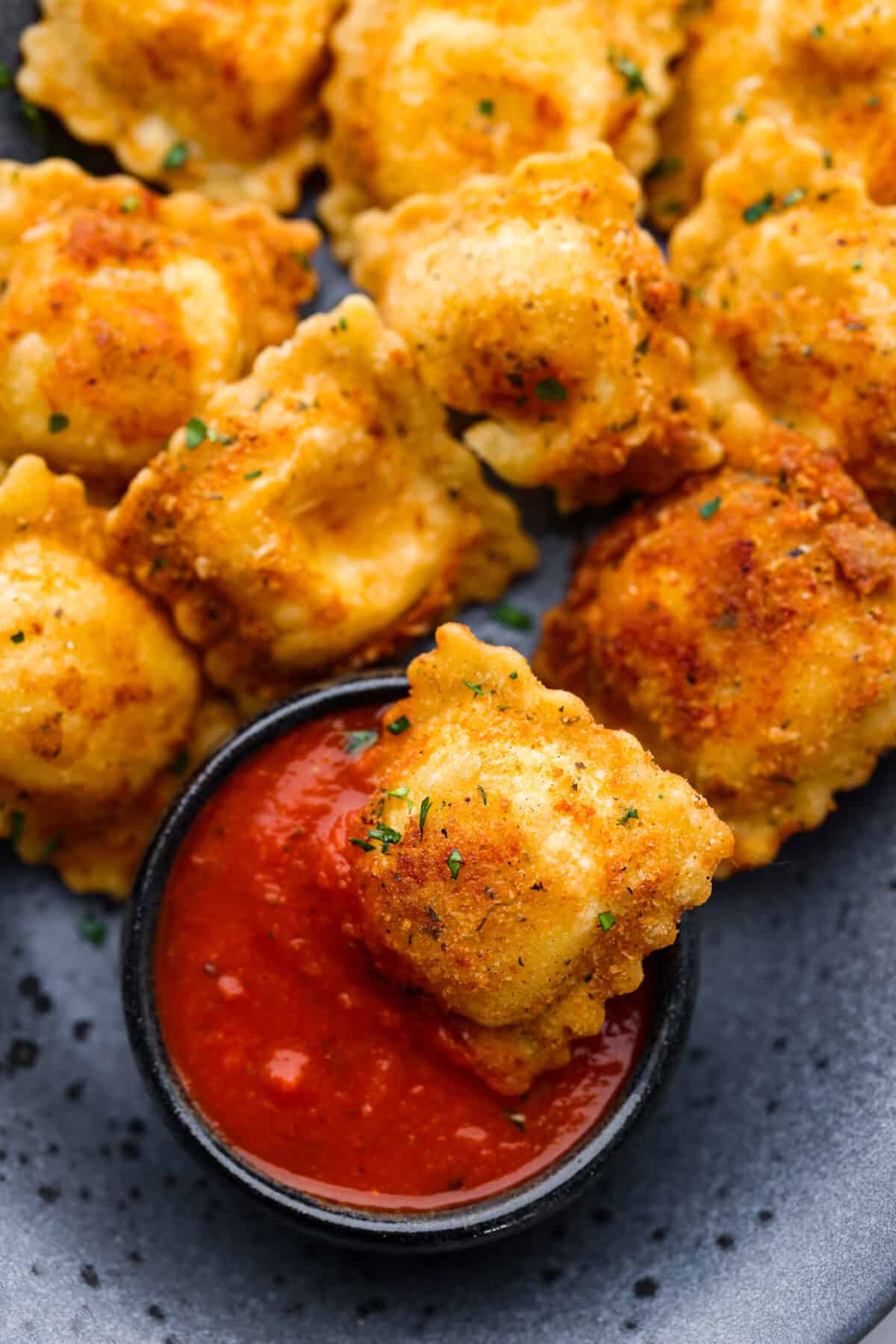 Tender ravioli coated in Italian breadcrumbs and parmesan cheese, toasted to golden brown perfection! Served with a side of marinara for dipping, this is one appetizer you donโt want to miss! A ravioli being dipped into marinara sauce.