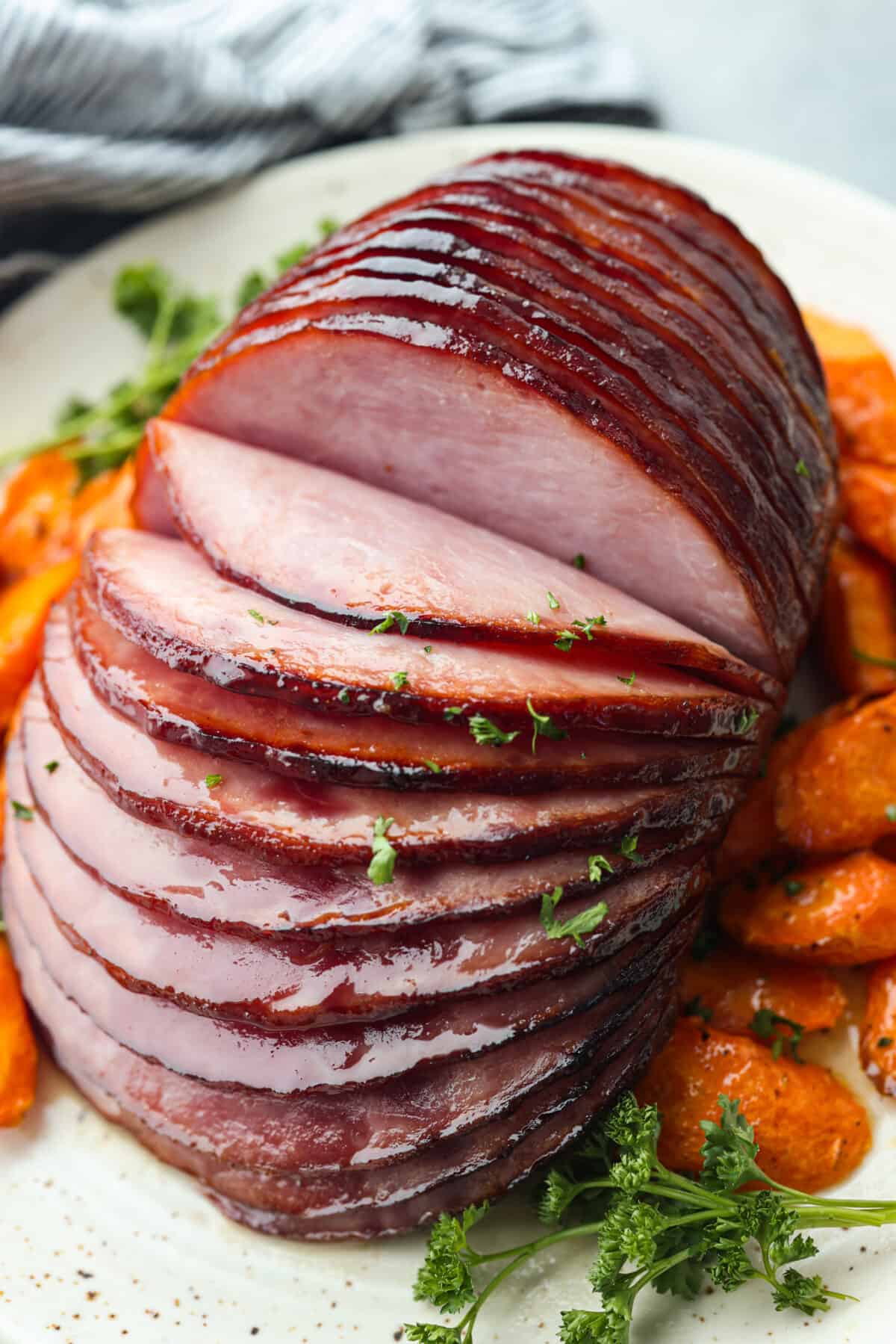 This air fryer ham is moist and flavorful with the most delicious caramelized honey glaze! It's super easy to make and tastes so incredible, you'll never want to cook ham any other way! Your friends and family will all be asking for the recipe! Closeup of a cut ham after being cooked in the air fryer. It is surrounded by sliced carrots.